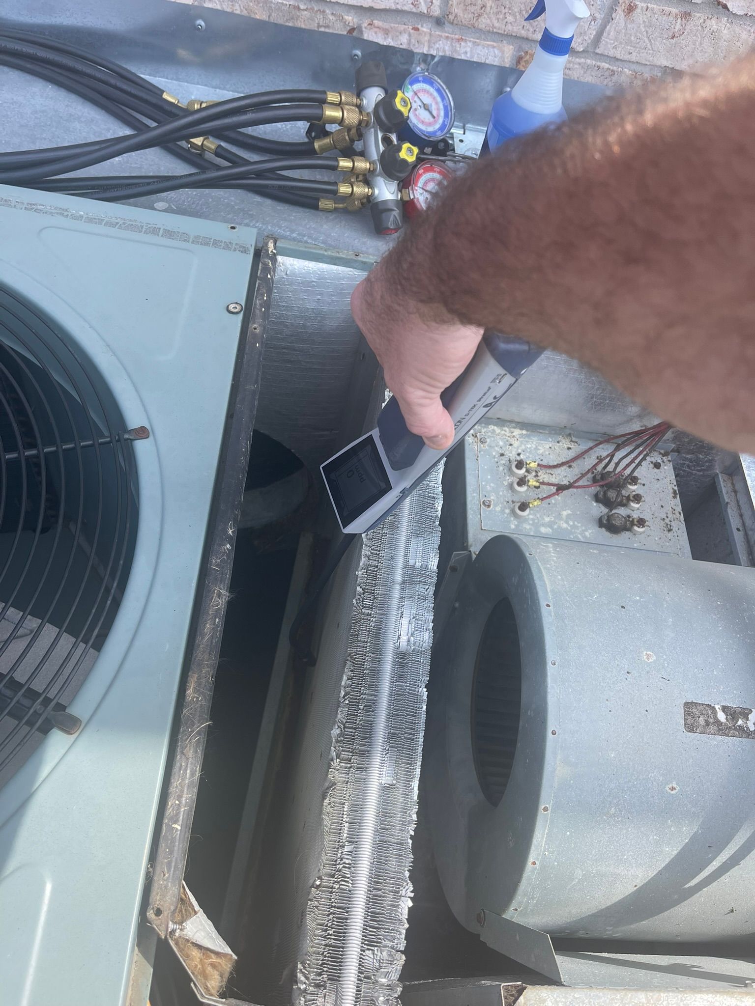 Hand reaching into an HVAC unit beside wiring, fan, and a cylindrical motor.