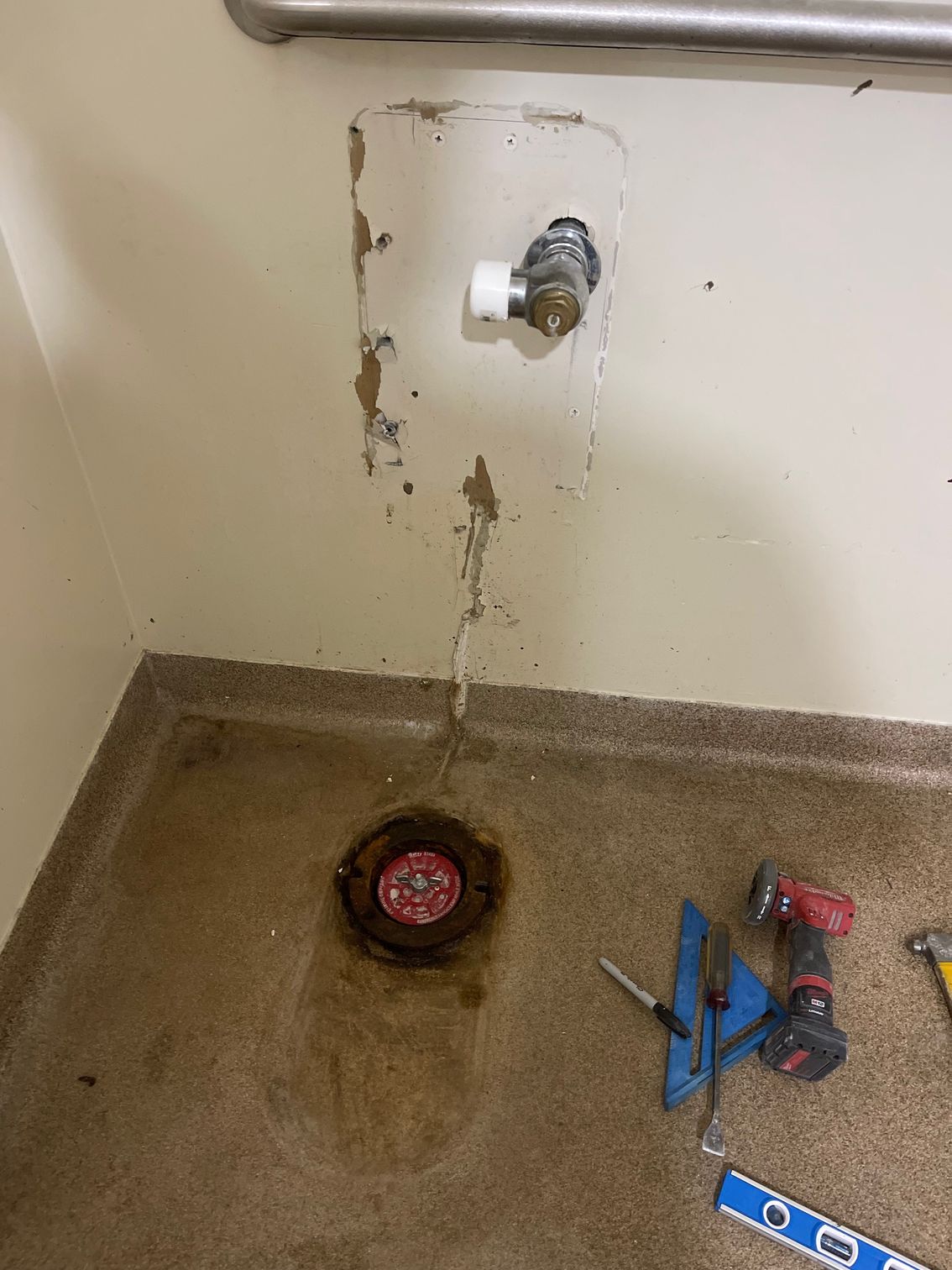 Water dripping from a wall faucet onto a floor drain, with tools on the wet floor.
