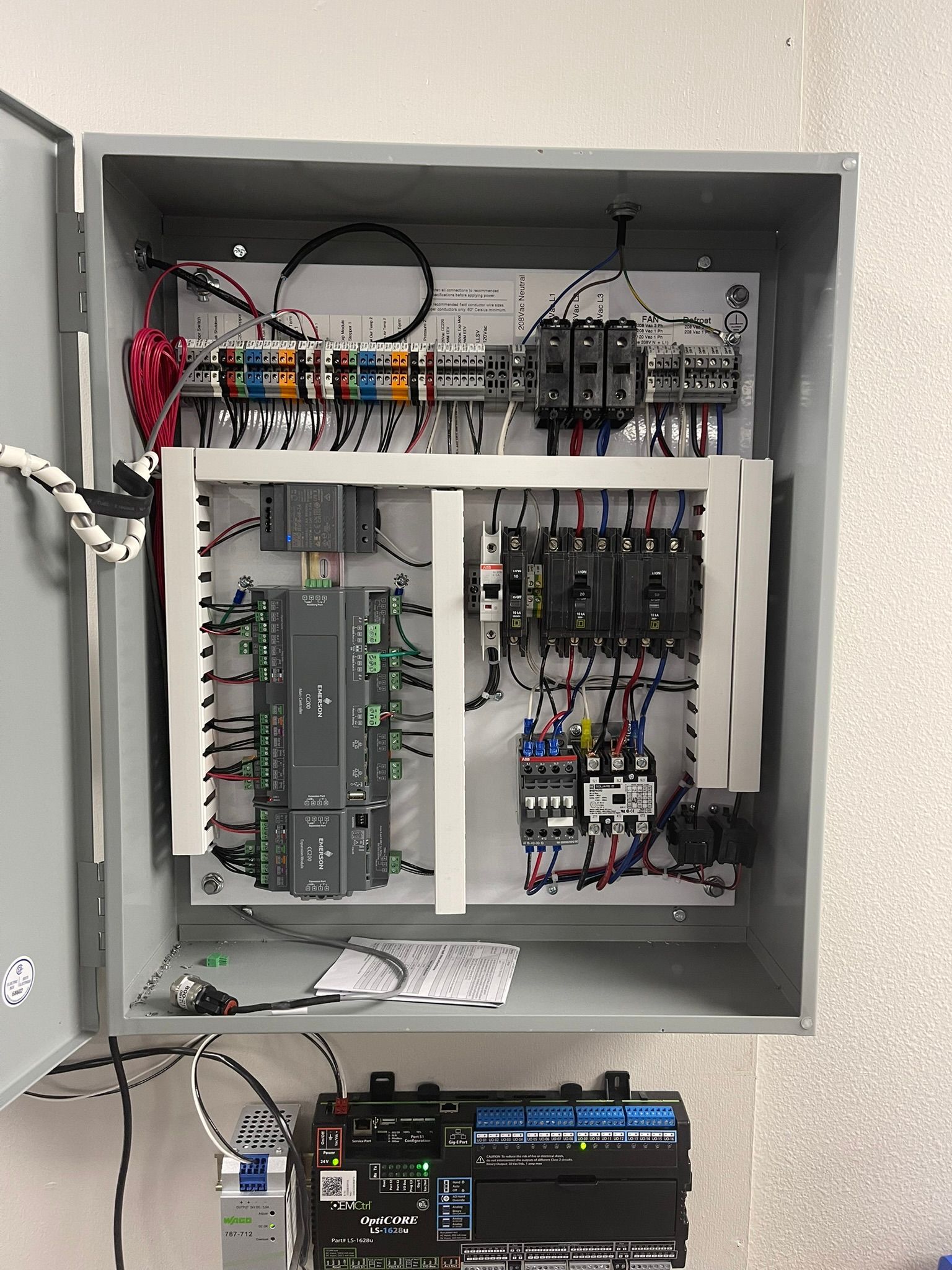 Open electrical control panel cabinet with wiring, circuit modules, and a small device mounted below.