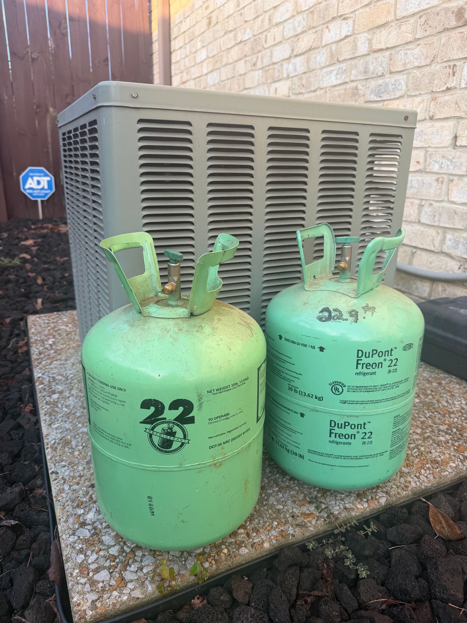 Two green gas cylinders beside an outdoor HVAC unit against a brick wall