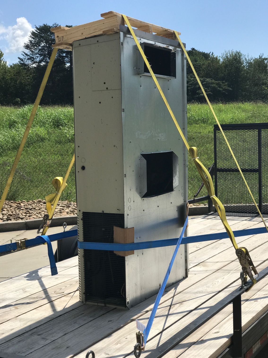 Tall gray test structure with straps and brackets on a concrete platform outdoors.