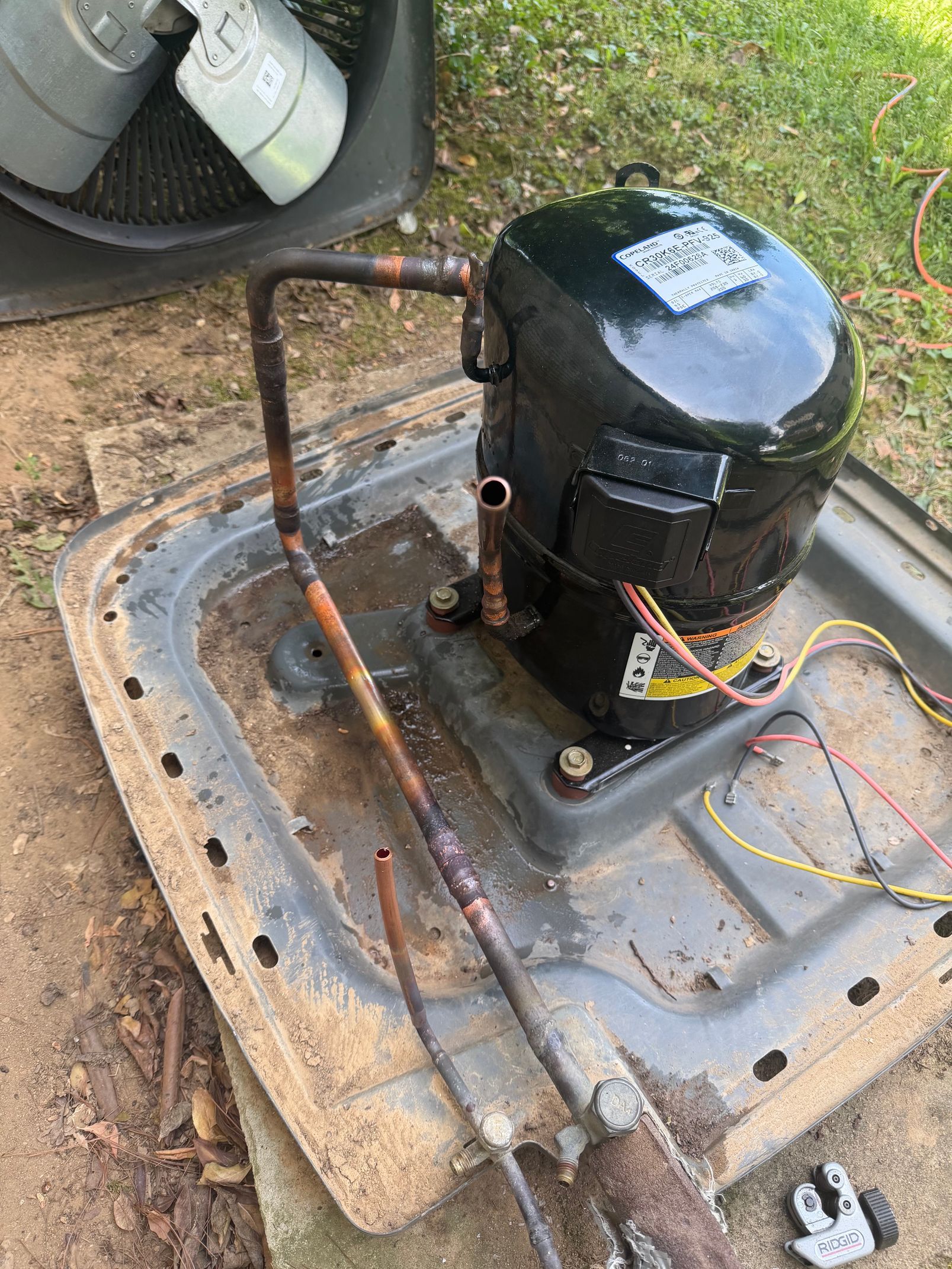 Outdoor HVAC compressor unit with copper piping and wires on a concrete pad beside grass