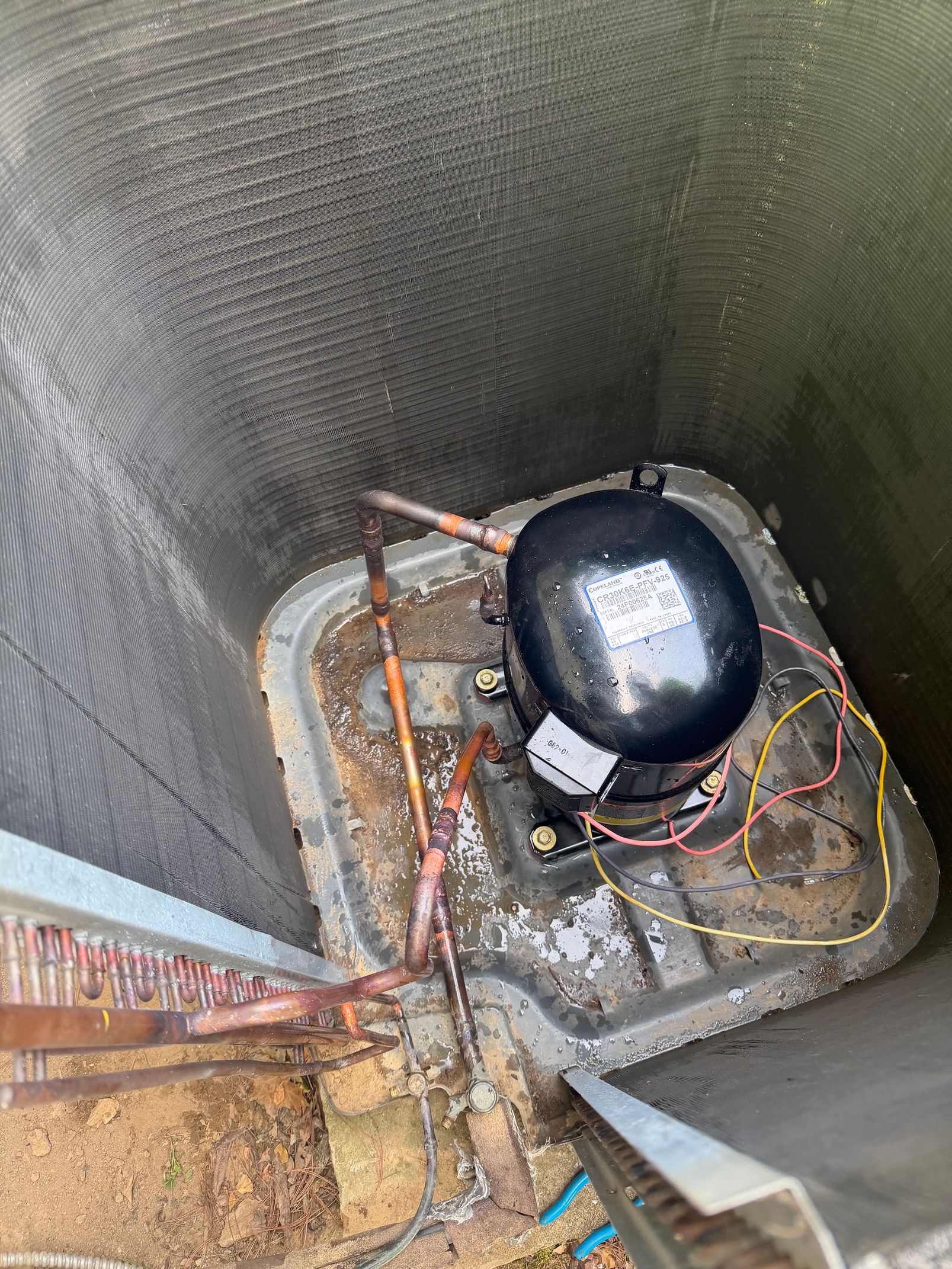 Utility pit with black tank, copper pipes, and wiring inside a concrete enclosure