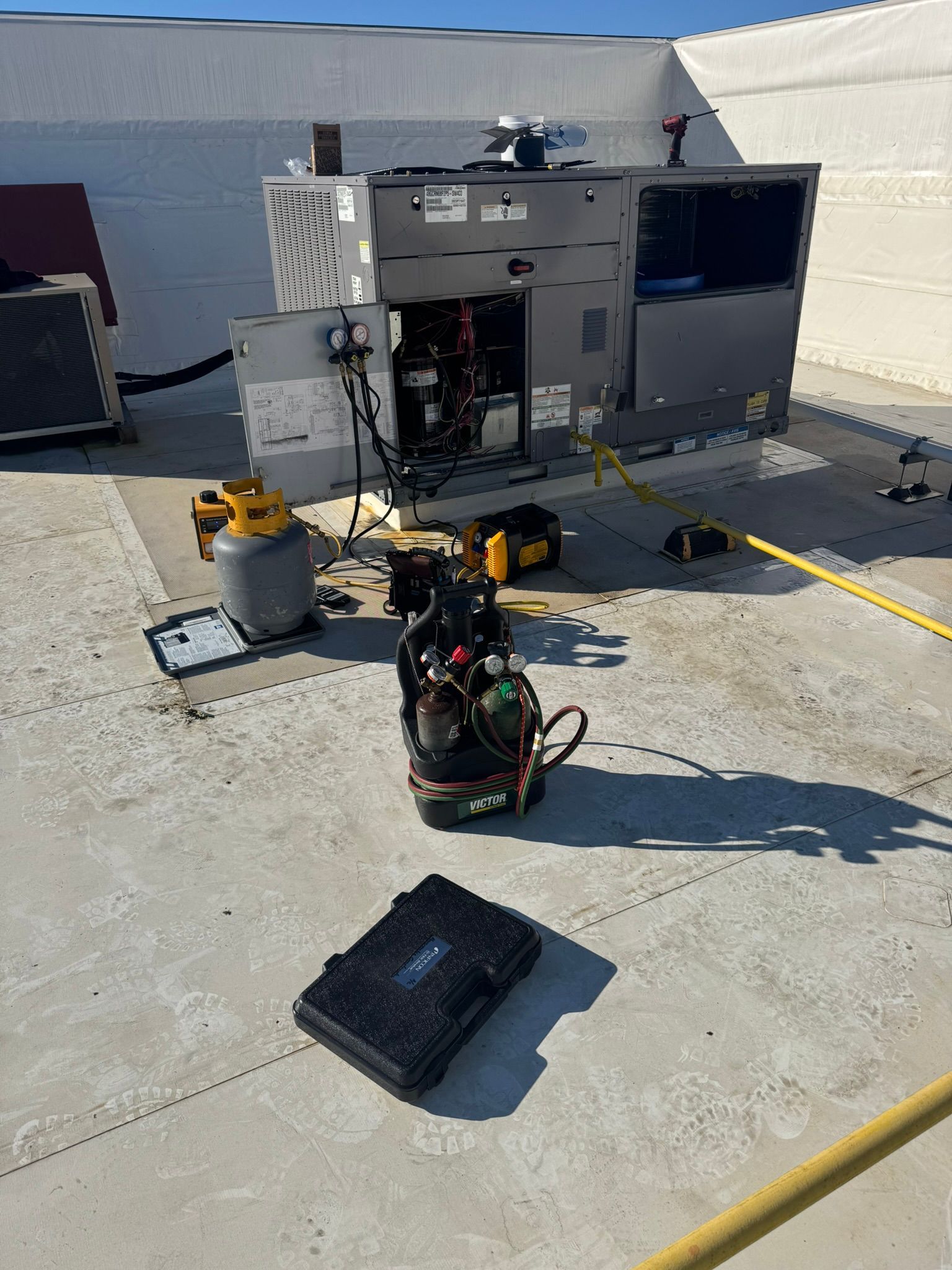 Industrial rooftop equipment with a scuba tank and gear on the ground beside an open HVAC unit.