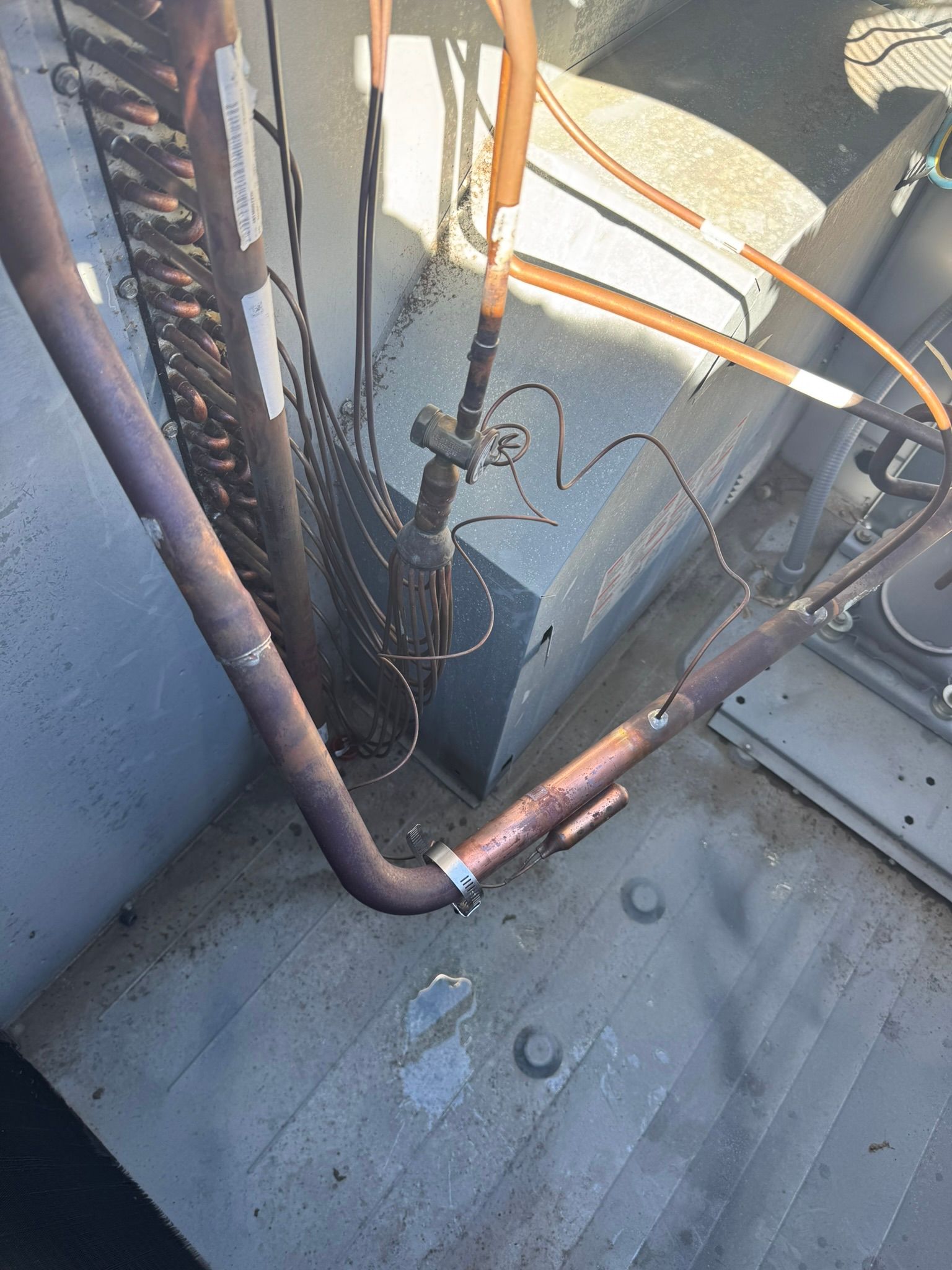 Rusty pipes and wiring in a rooftop utility area next to a metal surface.