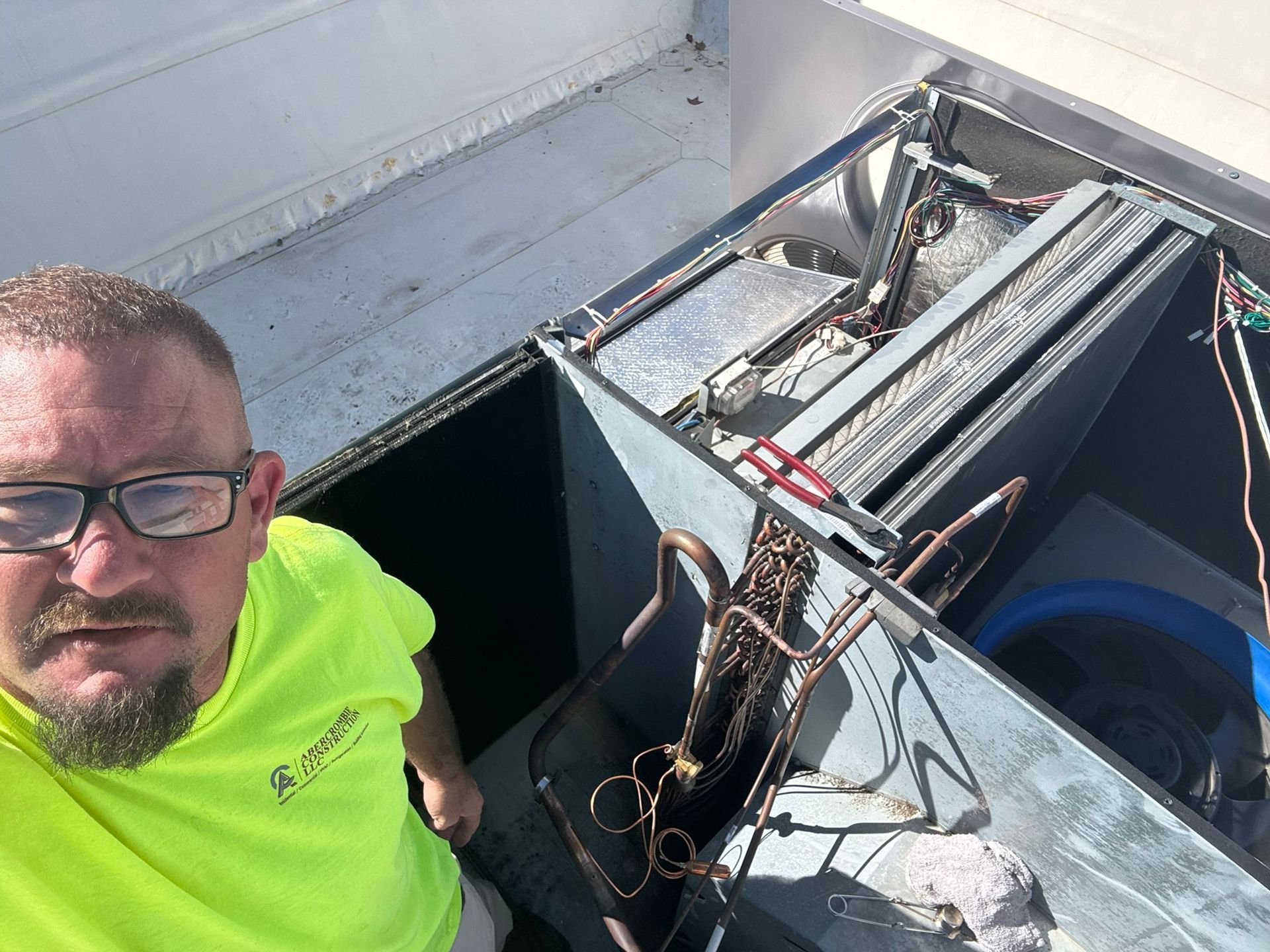 Man in neon yellow shirt beside open rooftop hatch with exposed electrical equipment