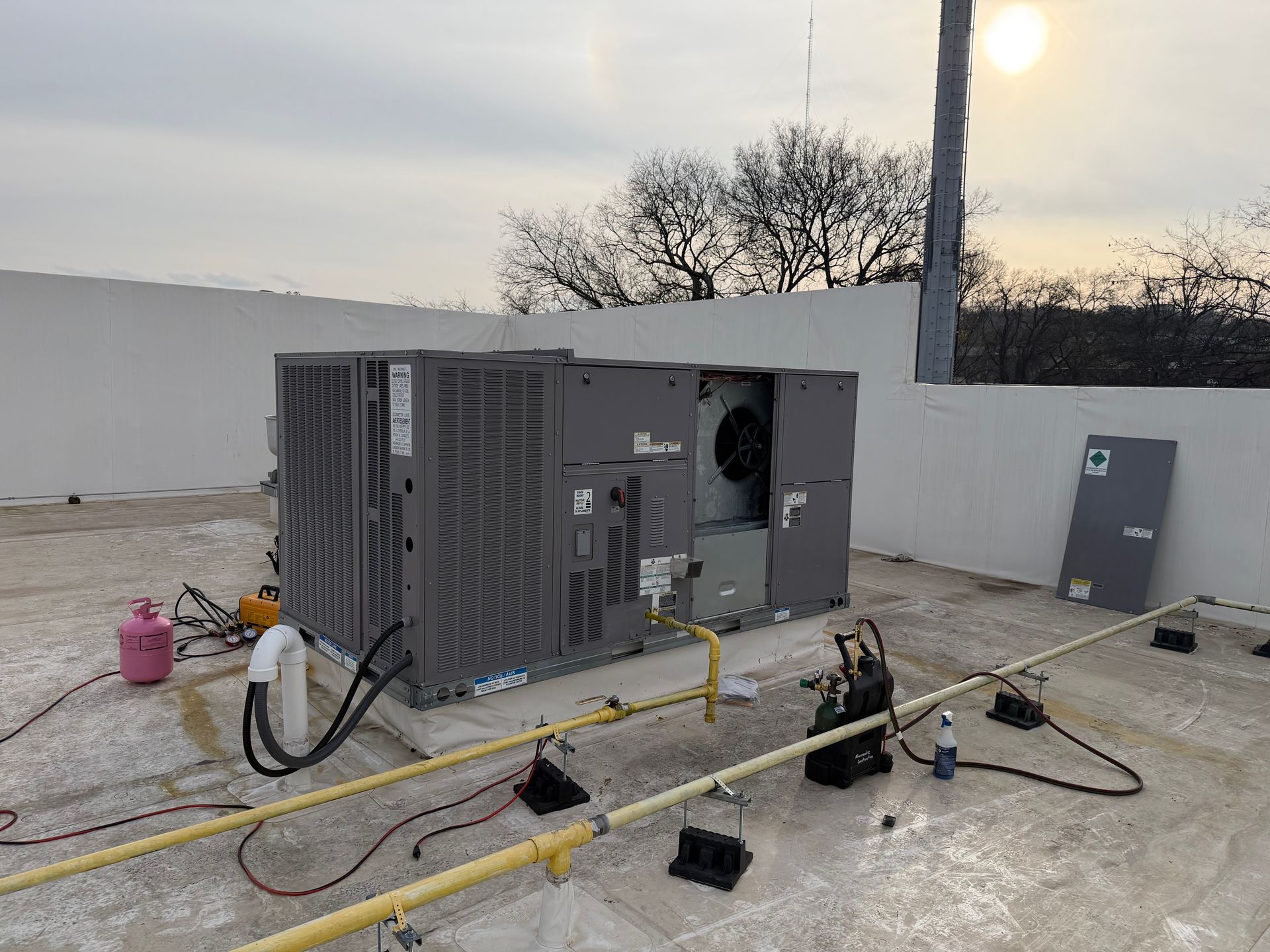 Outdoor HVAC unit being serviced with hoses and tools on a rooftop at sunset