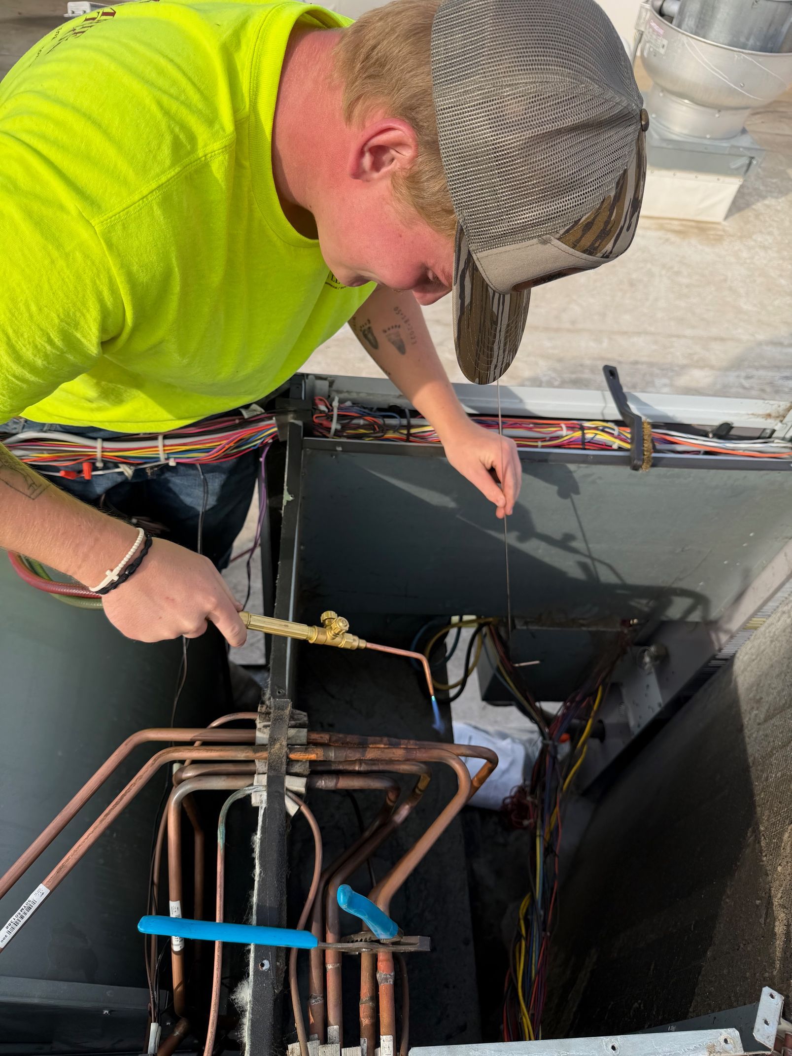 Technician in neon shirt inspecting pipes inside an HVAC unit outdoors