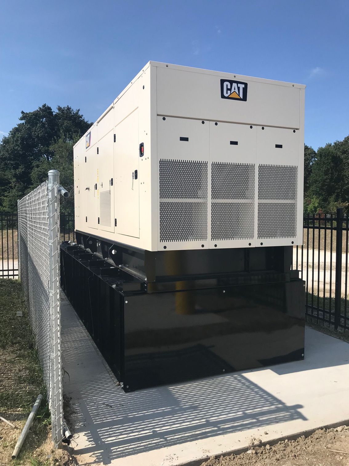 CAT generator on a raised black platform beside a chain-link fence and paved walkway.
