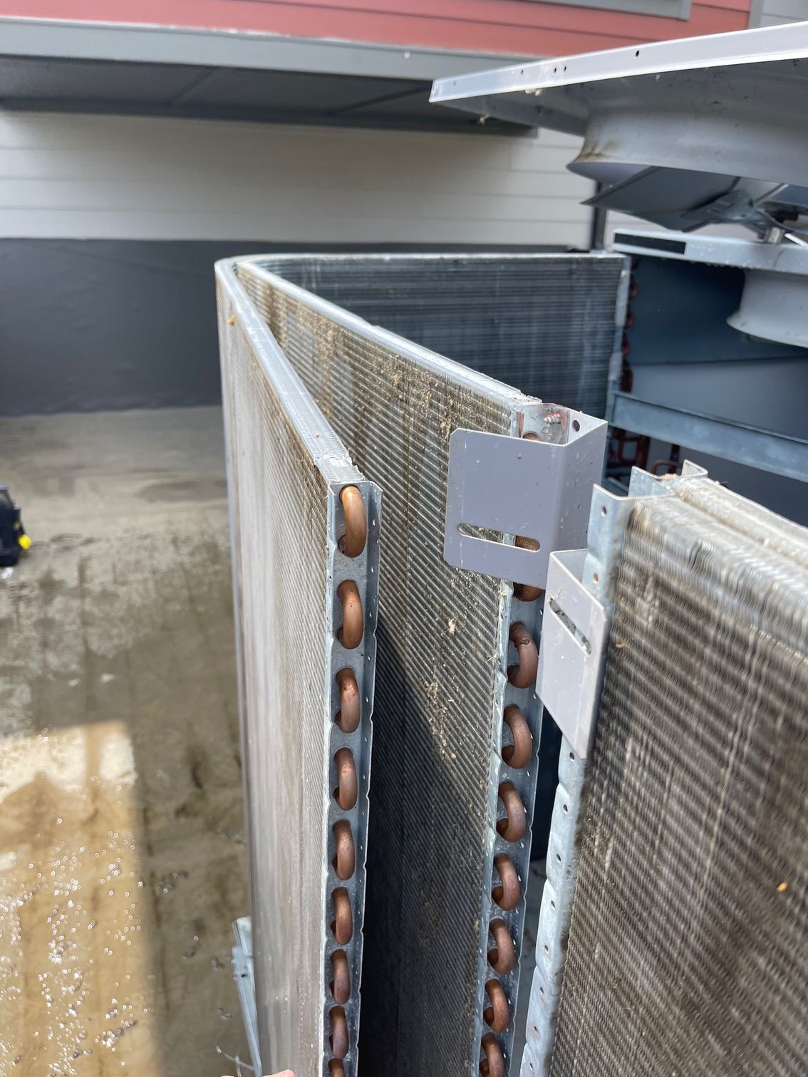 Close-up of an outdoor HVAC condenser coil with copper tubing and a metal mounting bracket.