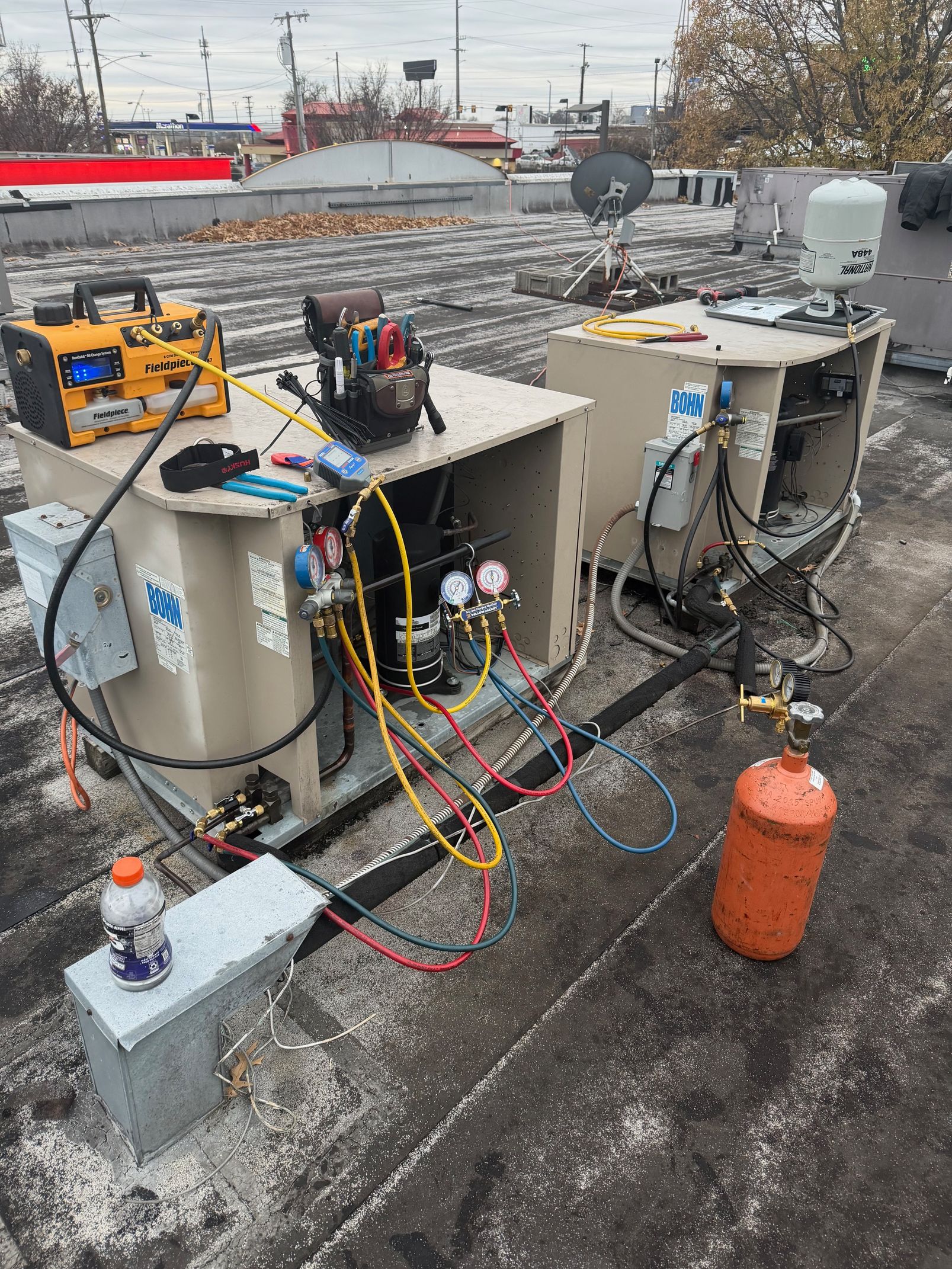 Industrial equipment and gas cylinders on a wet rooftop, with hoses and wires connected to machinery.