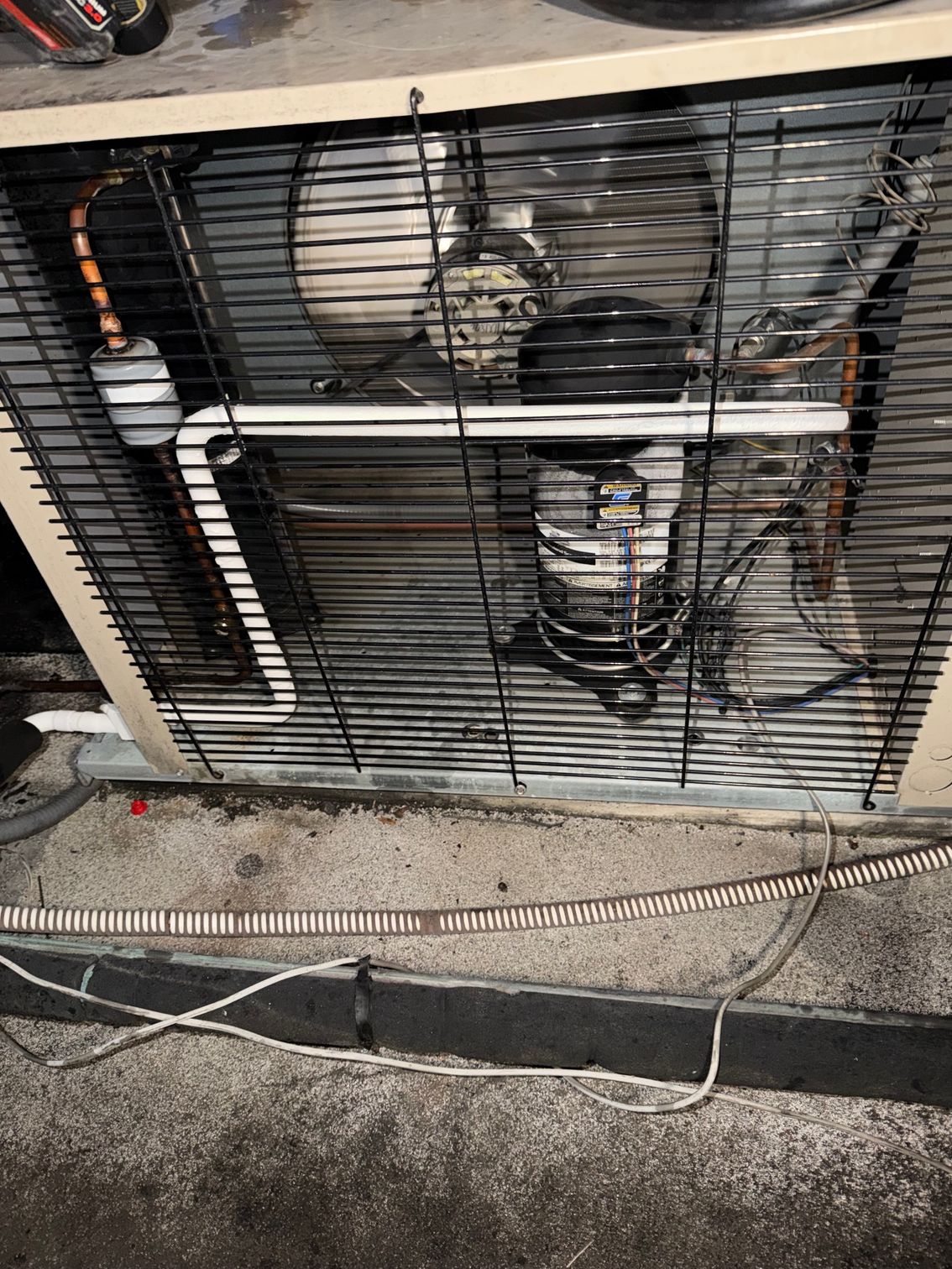 Damaged outdoor HVAC unit with bent metal grille and exposed fans, sitting beside a curb.