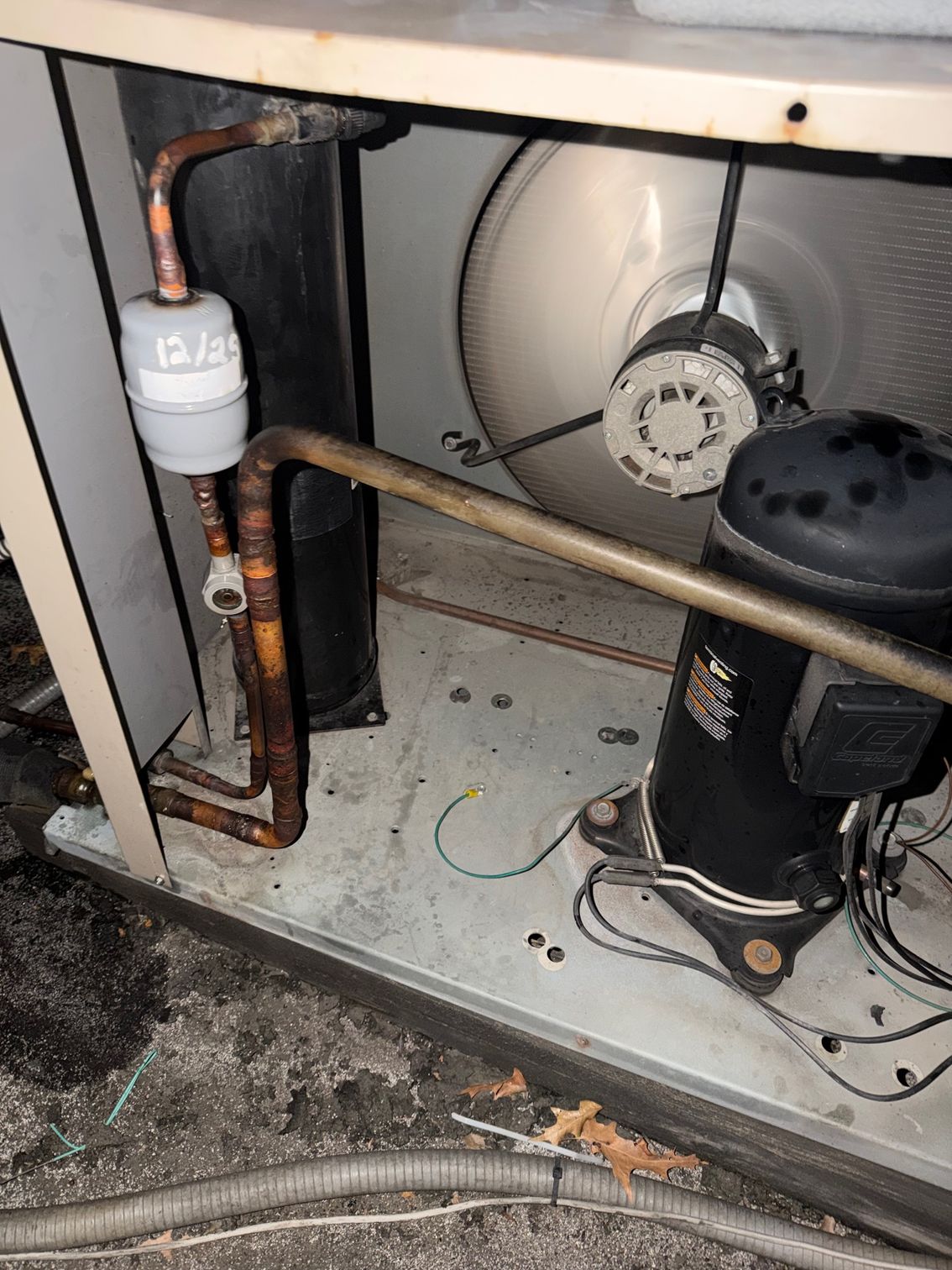 Open furnace compartment with copper pipes, black compressor, and dusty fan assembly.