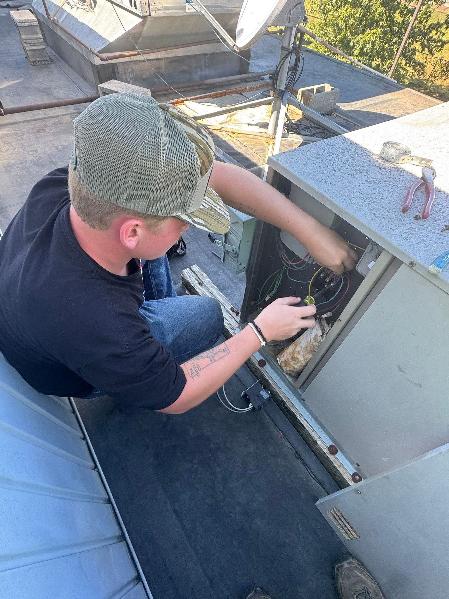 Person in a knit cap working inside an open rooftop hatch with tools.
