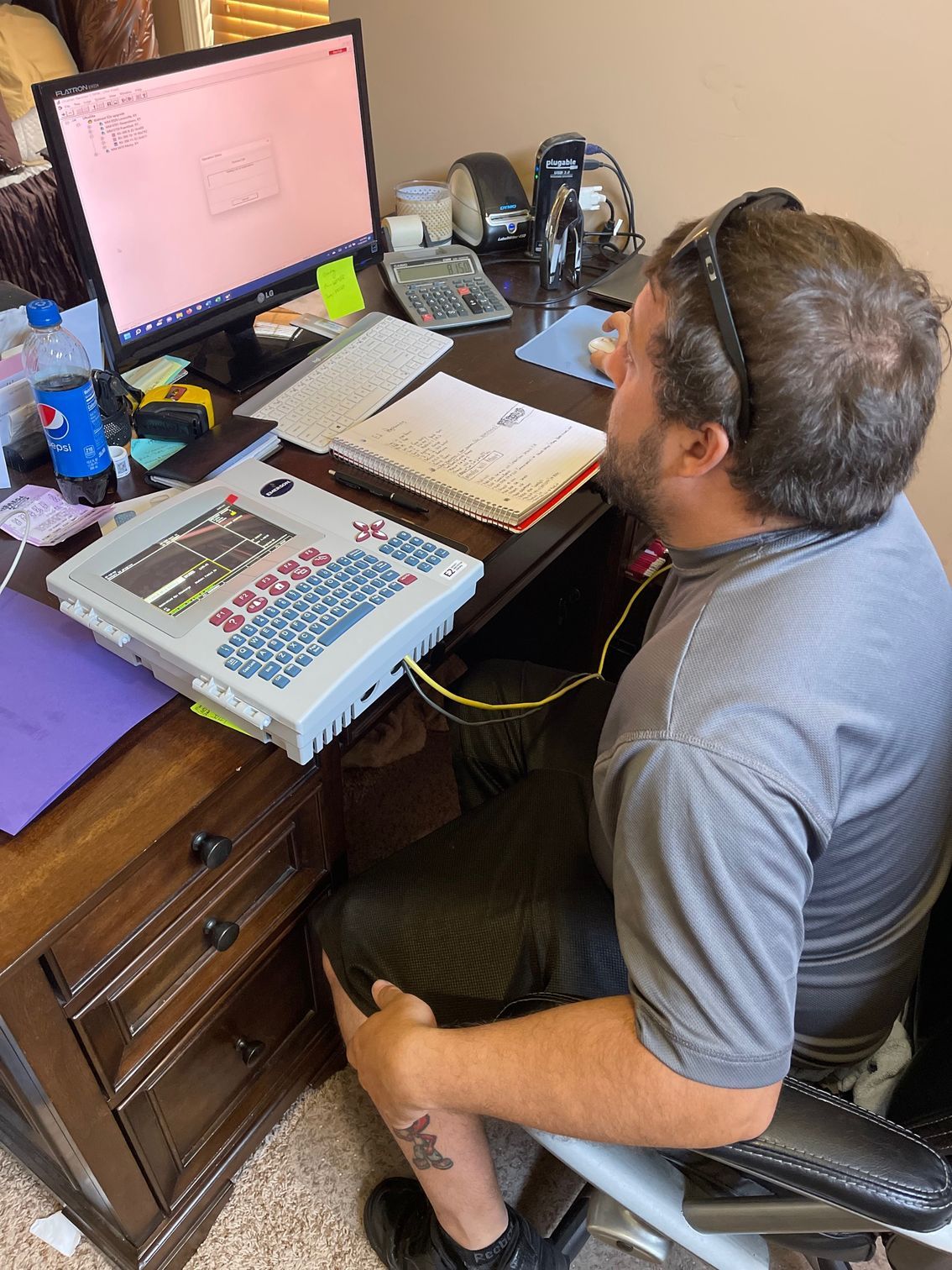 Person seated at a desk using a Braille embosser and computer monitor with pink screen.