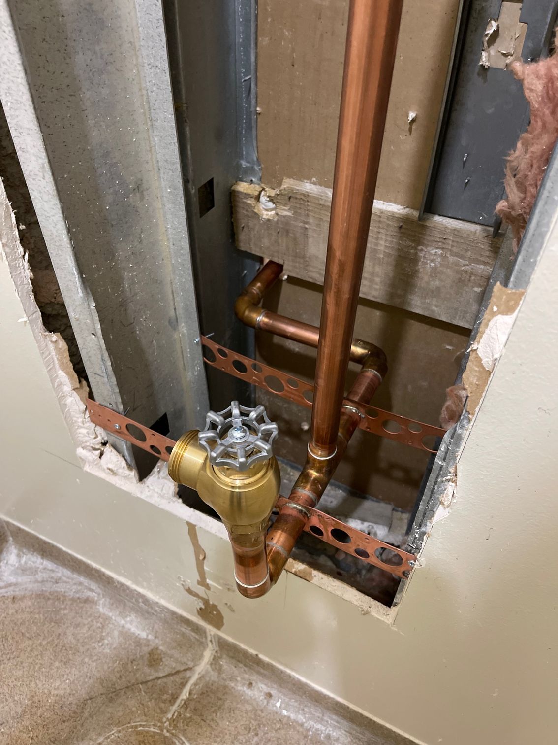 Open wall showing copper plumbing pipes and a water meter with brass fittings