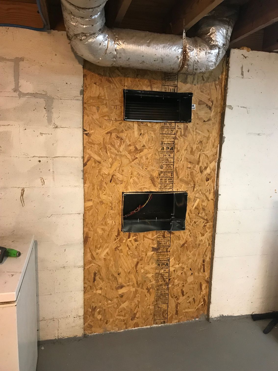 OSB-covered wall with two rectangular vents and silver ductwork in a basement-like room