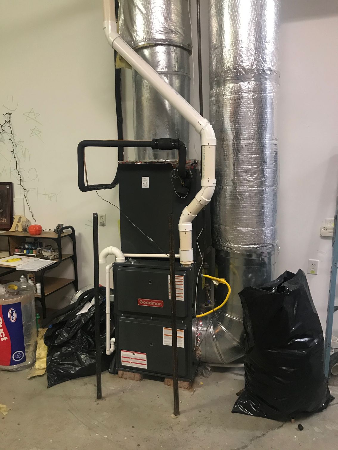 Home furnace/air handler with white ductwork and silver insulated vent in a basement utility area.