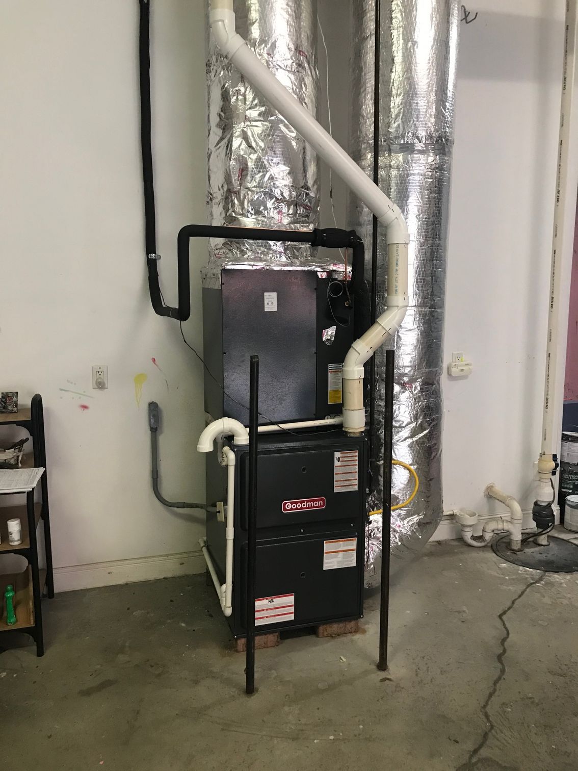 HVAC unit with white ductwork in a utility room against a concrete wall