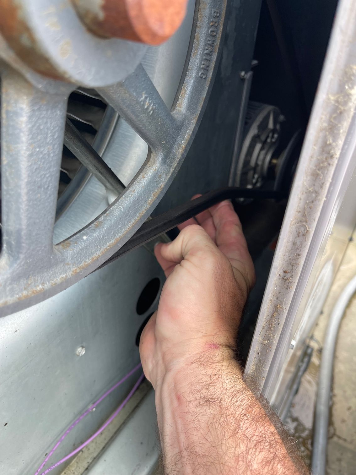 Hand reaching into a car engine bay near a belt and pulley assembly