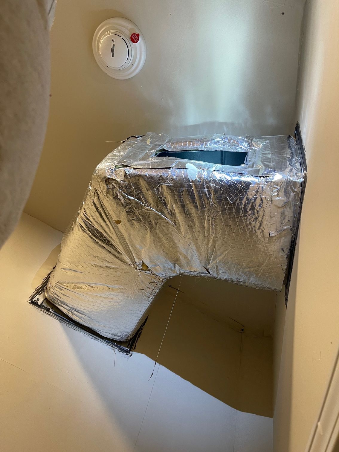 Wrapped ductwork in an unfinished attic with a smoke detector on the wall