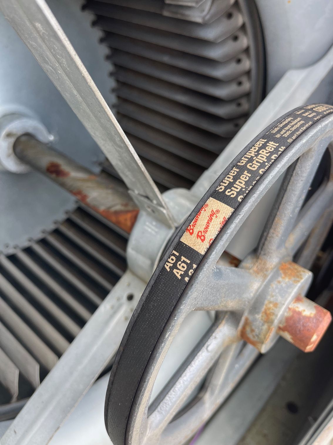 Rusty metal wheel and black belt on industrial machinery, with a gray ribbed fan in the background