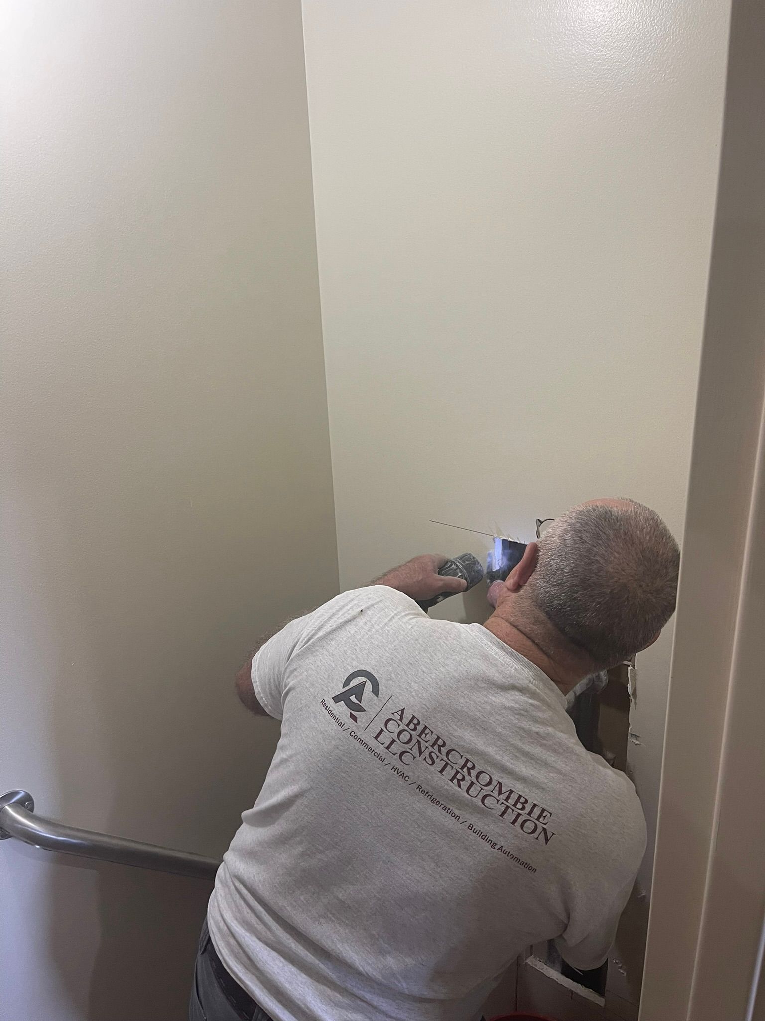 Person kneels on stairs, using a camera to photograph a blank wall corner.