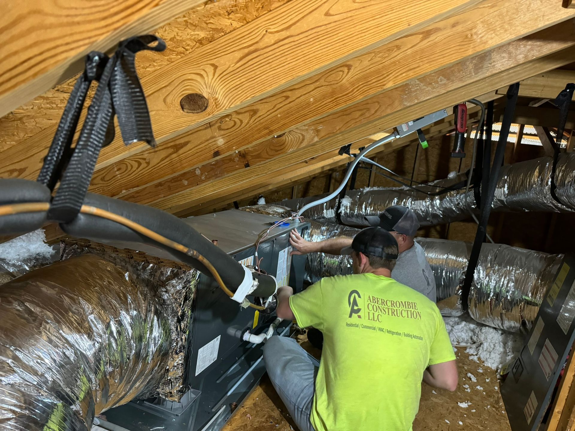 Technicians inspecting ductwork in a crawlspace under exposed wooden beams