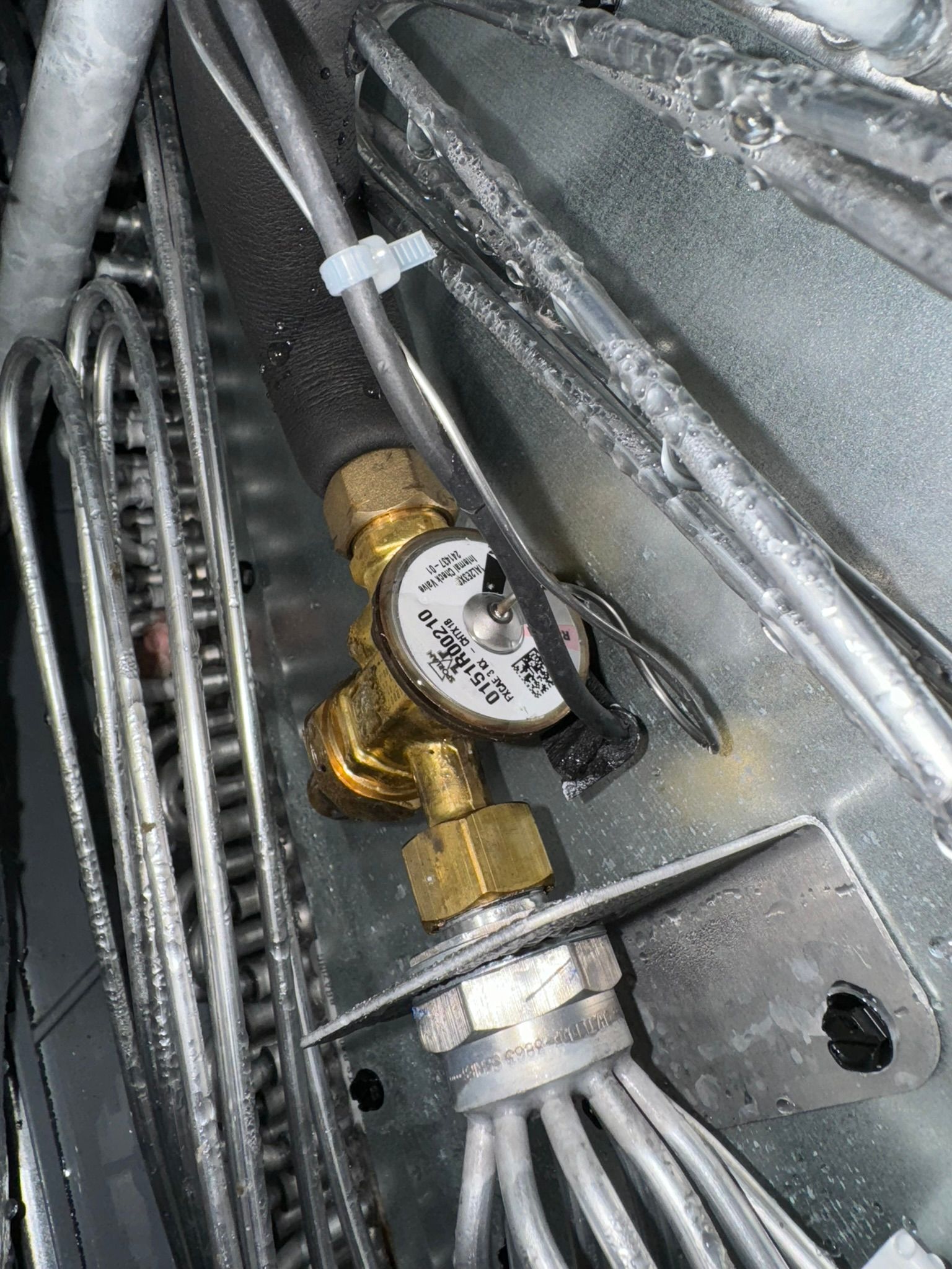 Brass shutoff valve on a pipe inside a metal wall cavity with bundled cables