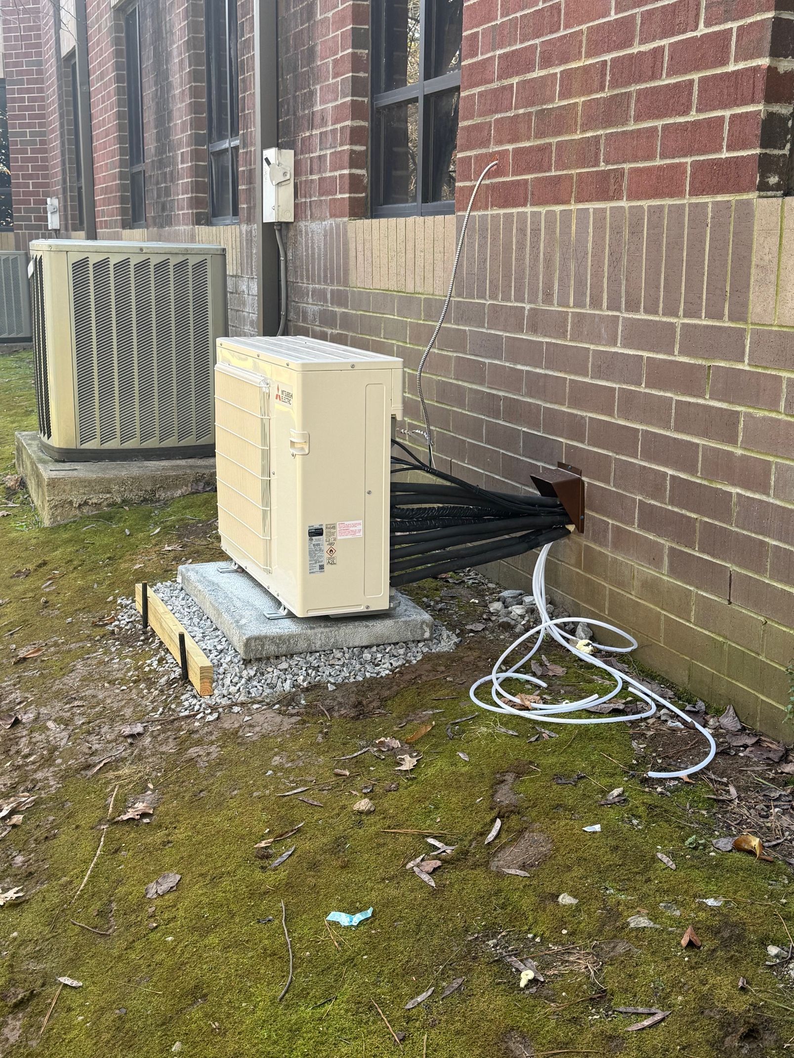 Outdoor HVAC units beside a brick building with exposed cables and patchy grass.