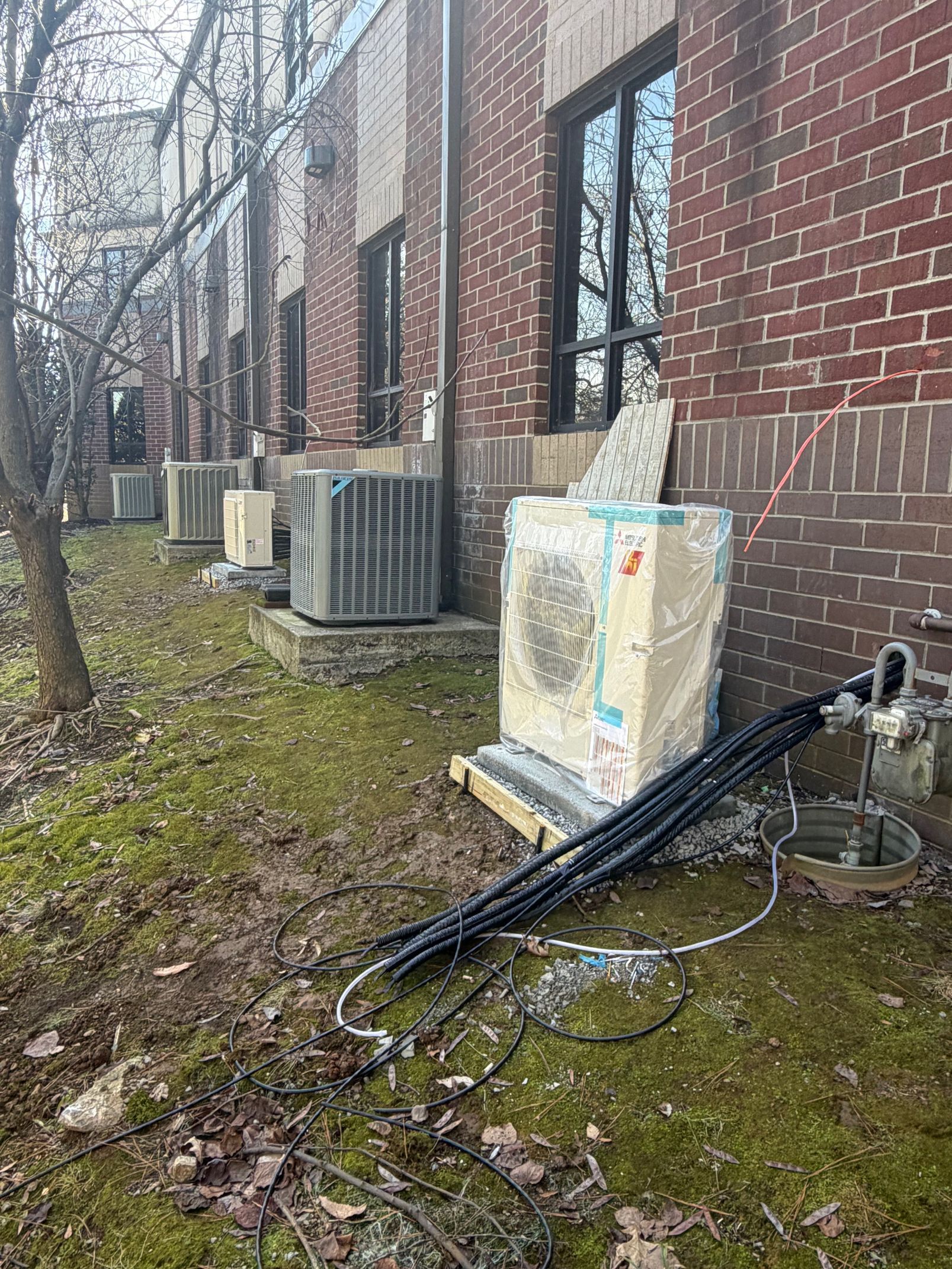 Outdoor utility area beside a brick building with HVAC units, pipes, and a fallen black pole on the ground