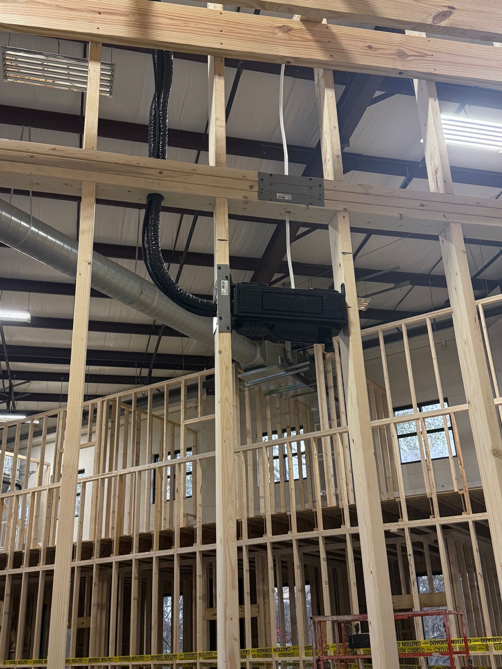 Construction framing with exposed wooden studs, ceiling beams, and black ductwork in an unfinished interior