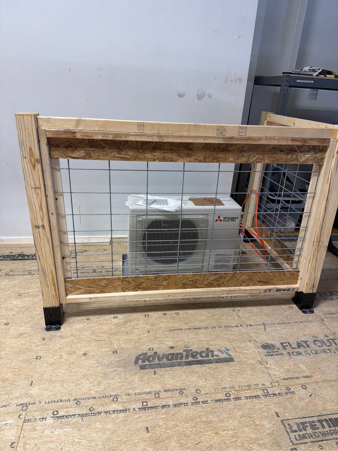 Wooden-framed wire cage with a small white air conditioner inside in a utility room.