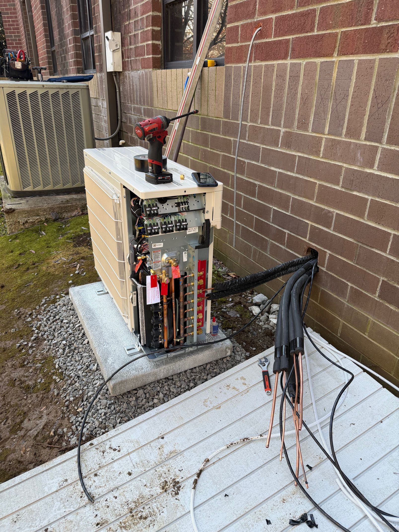 Outdoor electrical control box beside a brick wall, with cables and a snow-dusted ground nearby.
