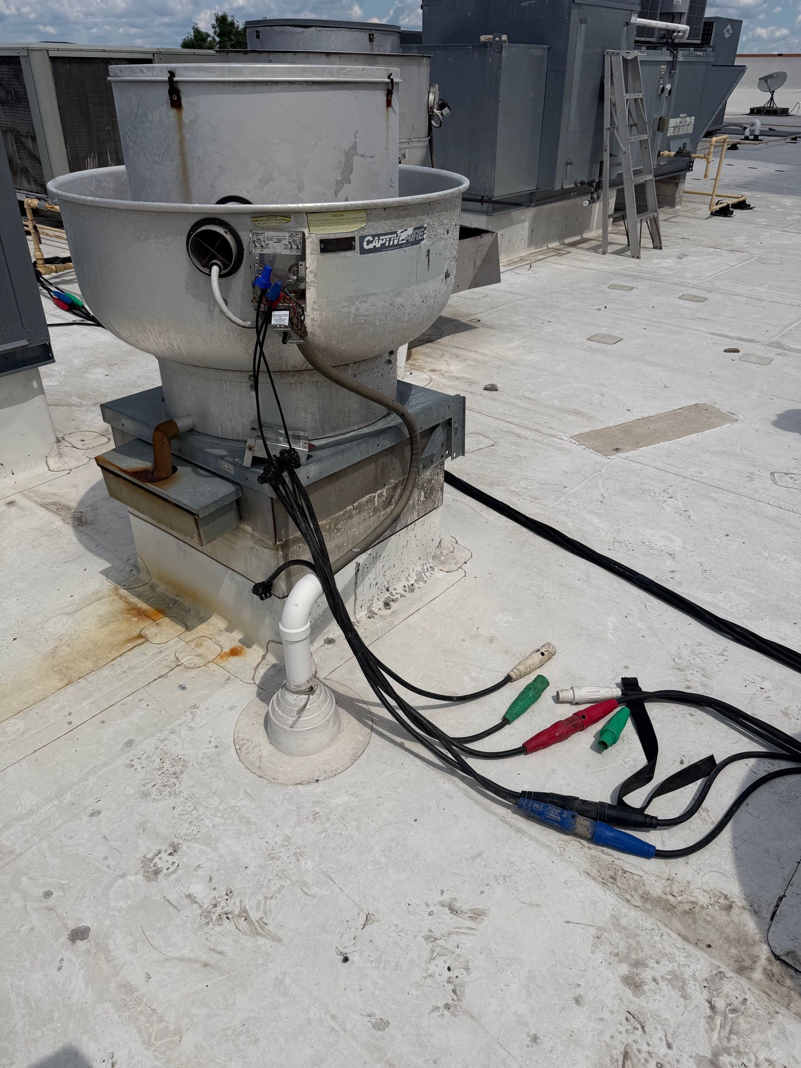 Industrial equipment with black and colored cables on a concrete rooftop, near metal tanks and pipes