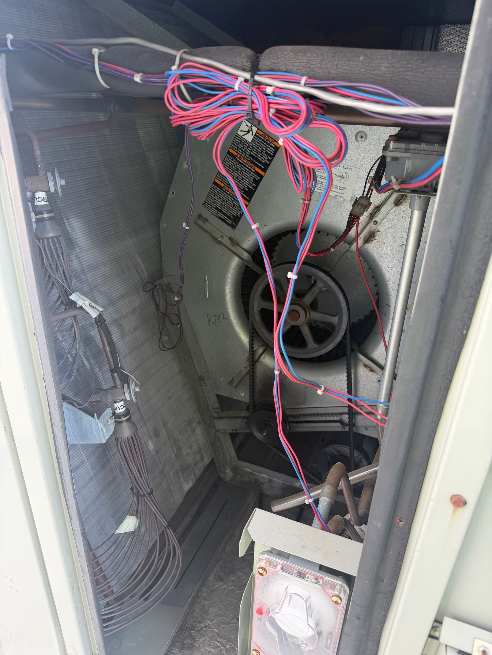 Open HVAC unit with exposed wiring and a large circular fan inside a metal cabinet.