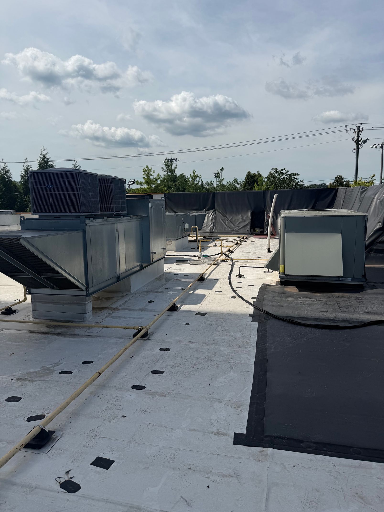 Rooftop with HVAC units and ductwork under a cloudy sky, with a dark repair patch on the roof.