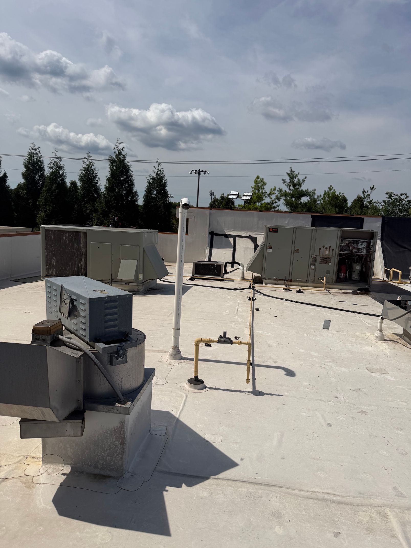 Rooftop with HVAC units, vents, and pipes under a cloudy sky, with trees in the background