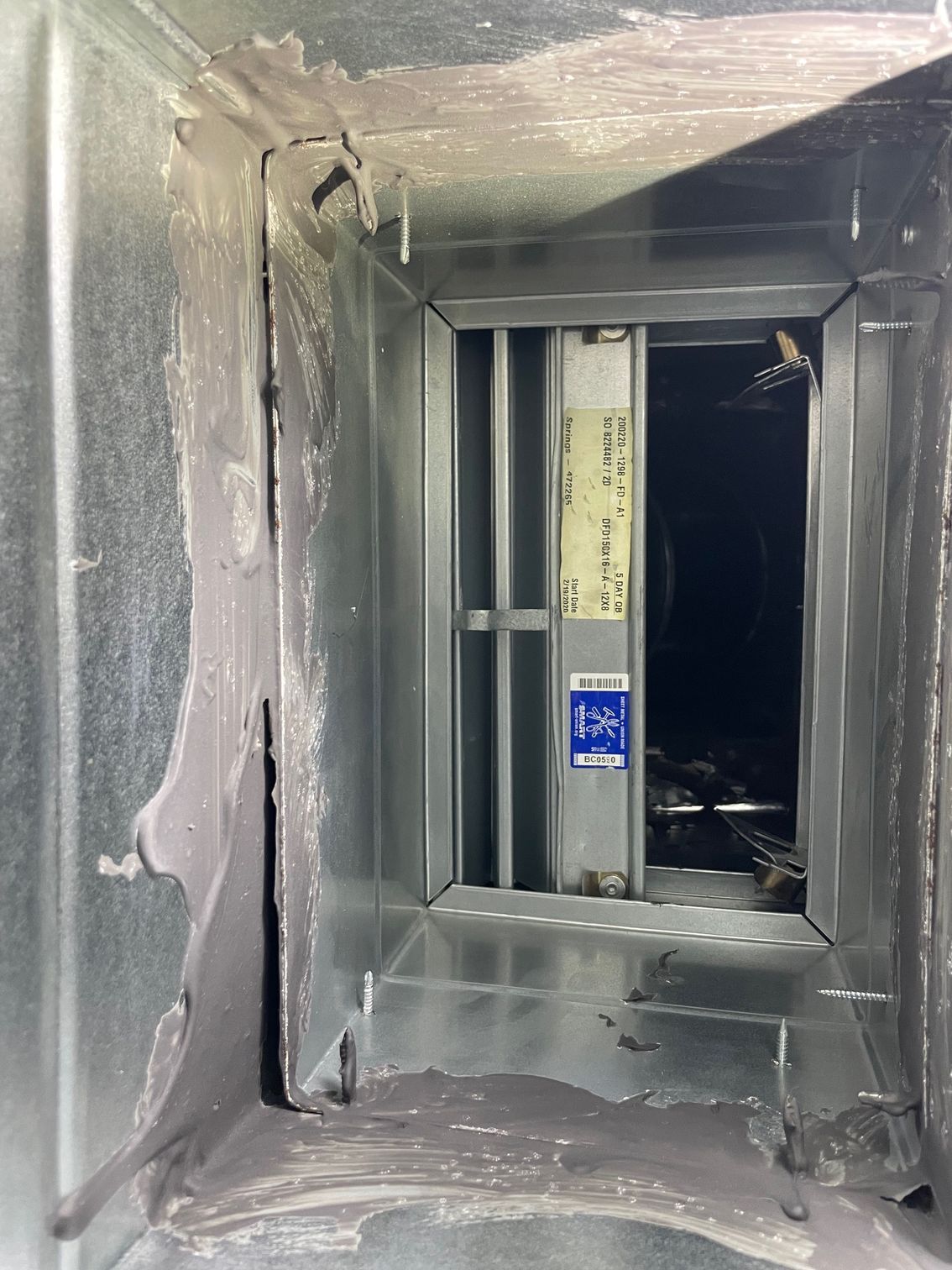 Gray metal air duct interior with a rectangular opening and dark passage beyond, showing insulation residue.