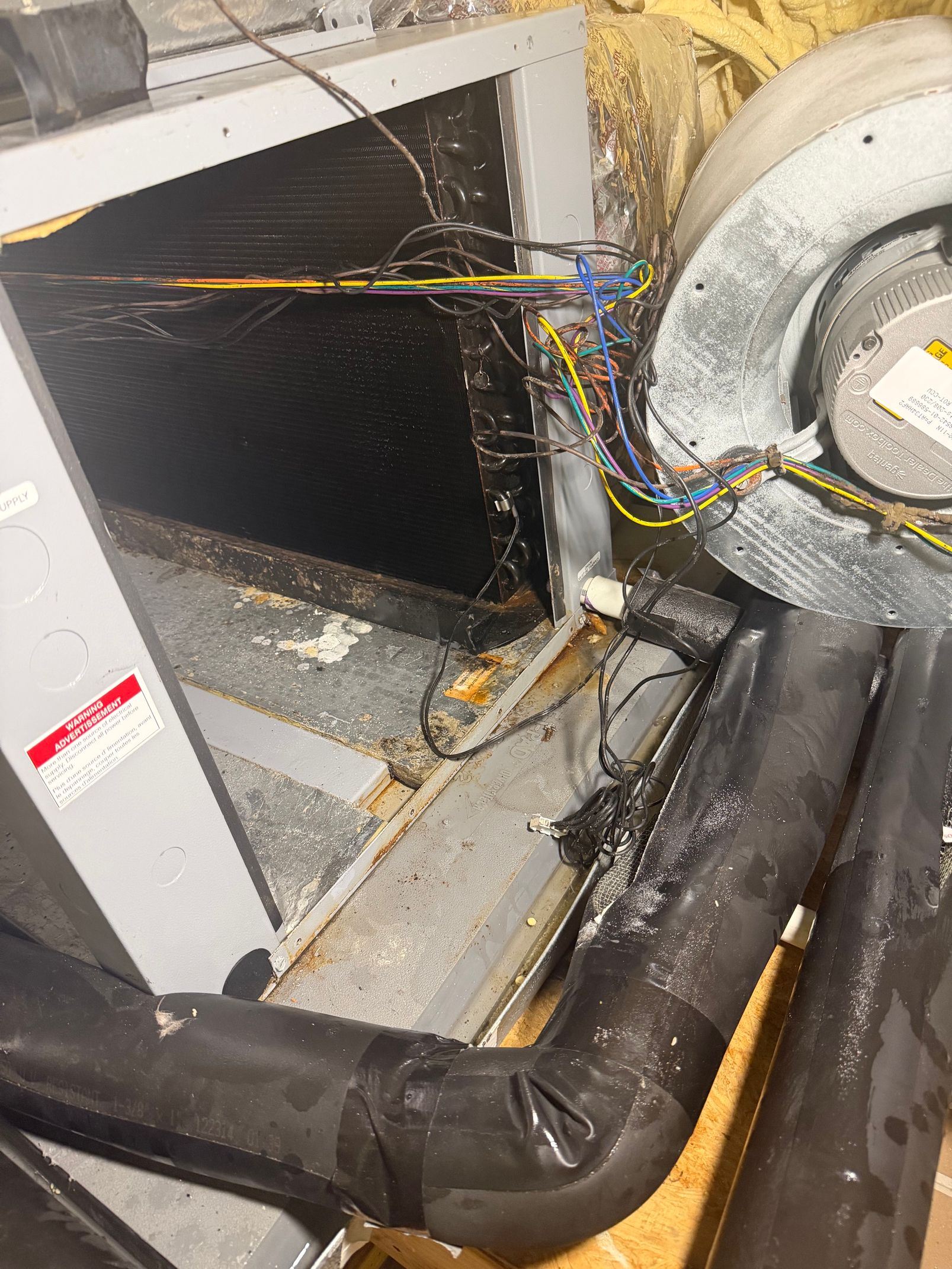 Damaged HVAC unit with exposed wiring and insulated ducts in a utility space