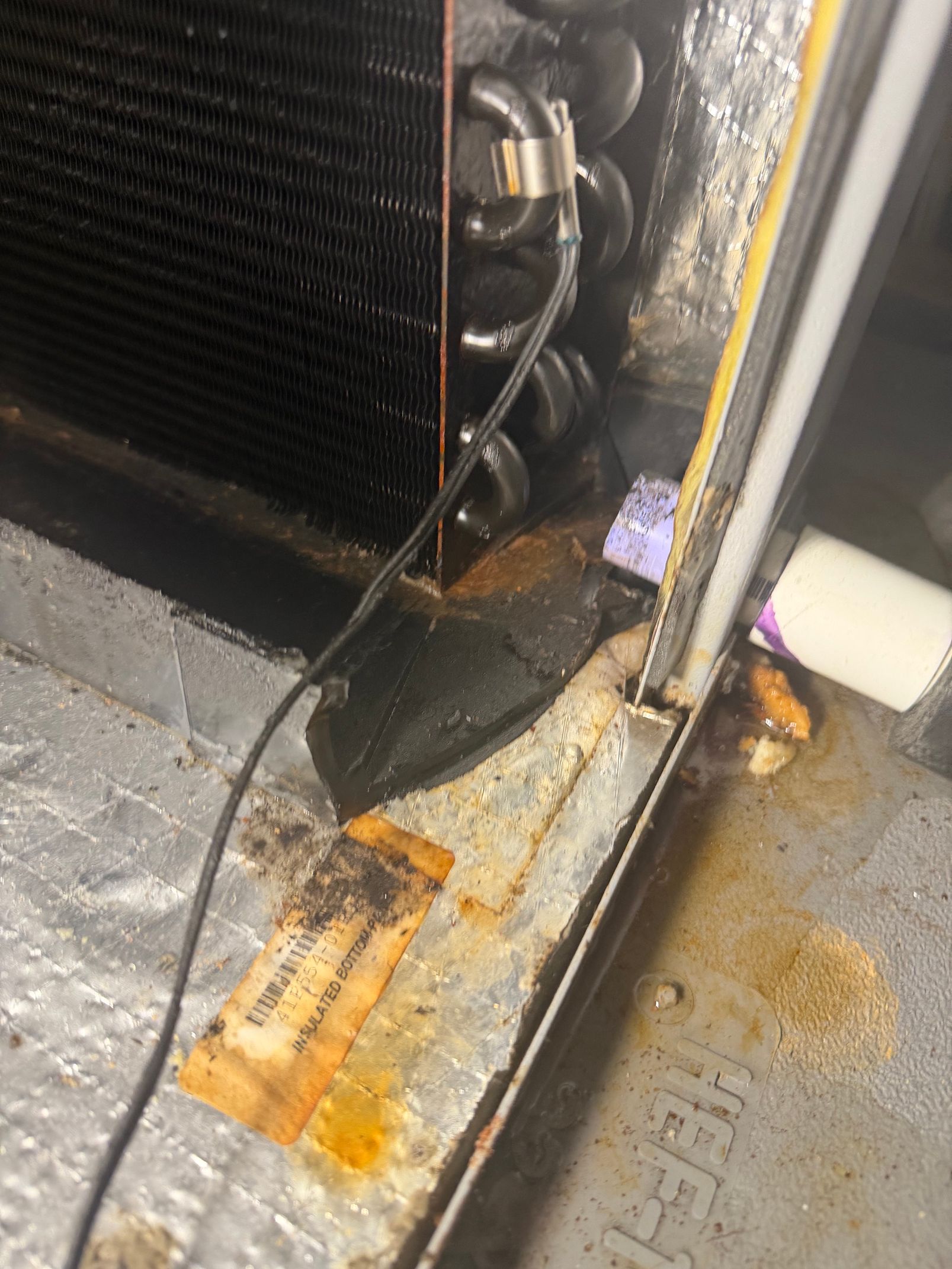 Rusty appliance corner with water damage and stained floor near a black coil and hose