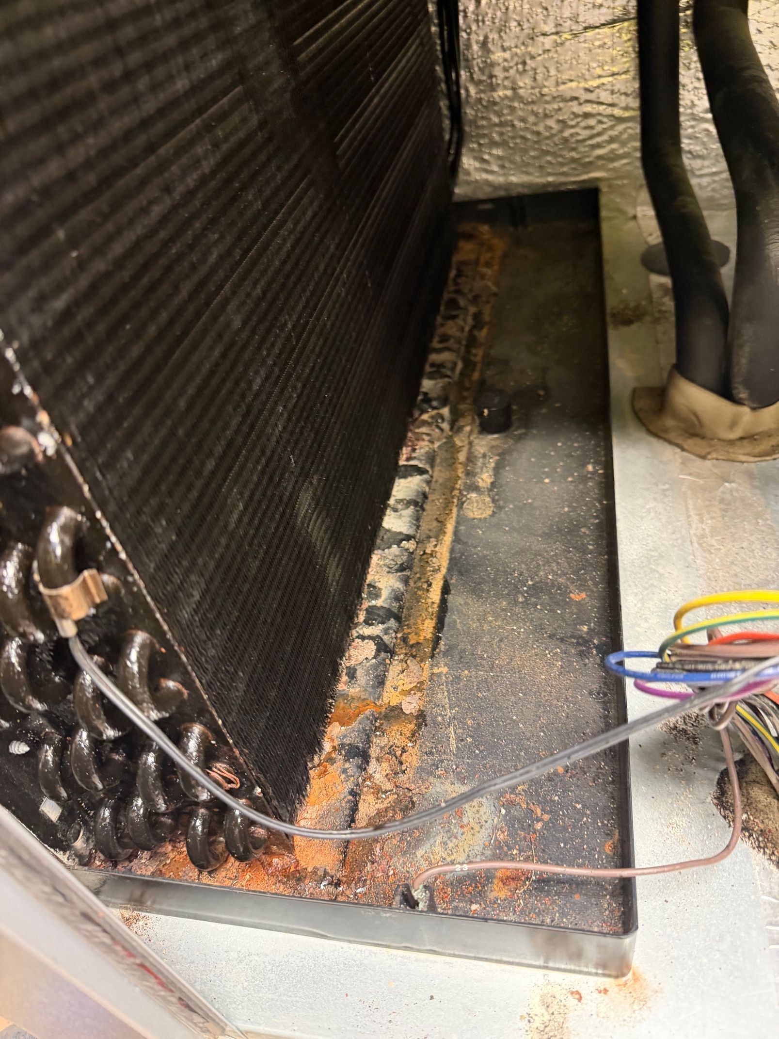 Dusty HVAC condenser coil and base with debris and exposed wires on a concrete floor