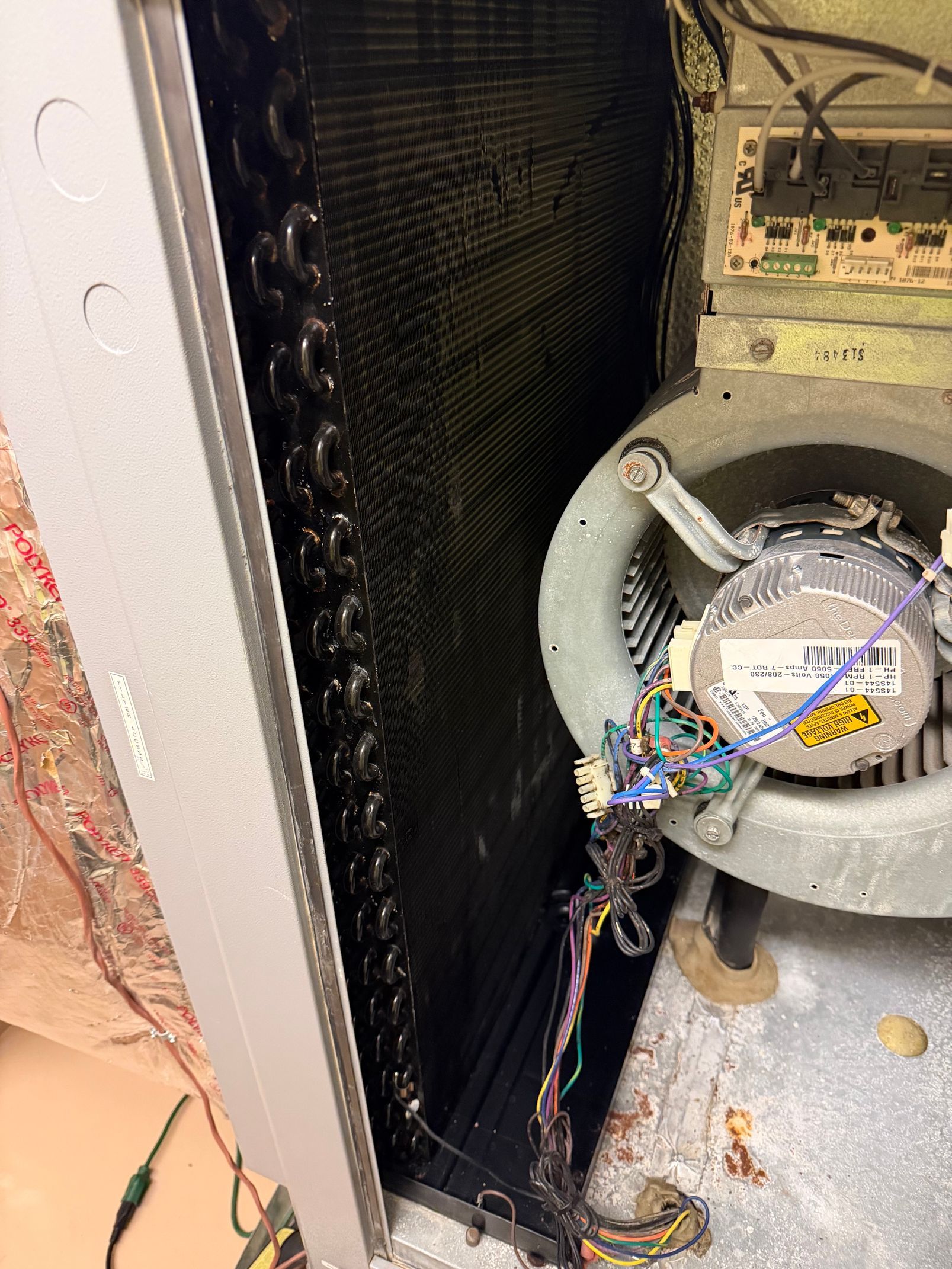 Open electrical compartment with exposed wiring, fan housing, and debris inside a metal appliance.