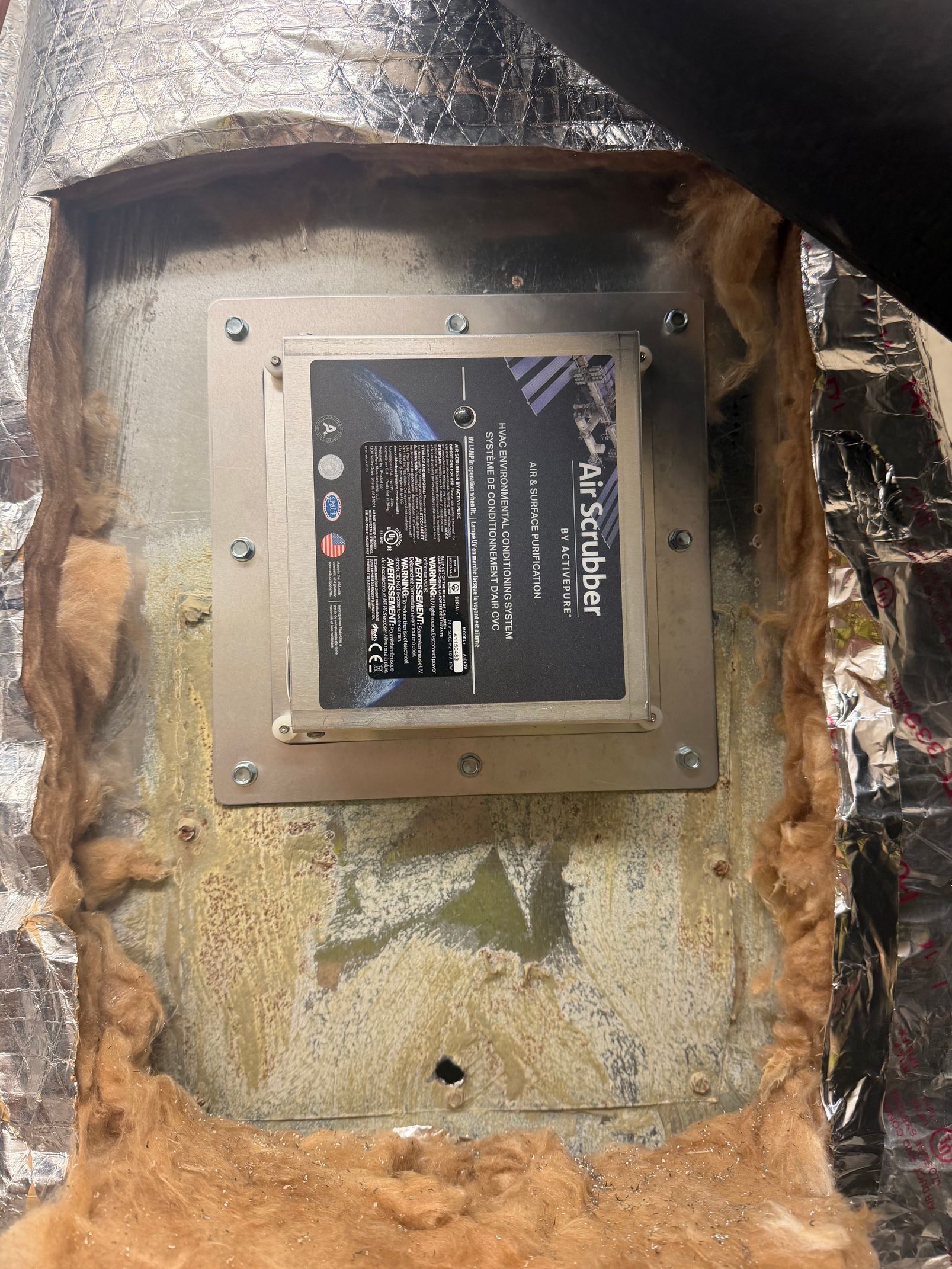 Damaged wall with a small framed plaque or device mounted in a rough, burnt-looking opening.