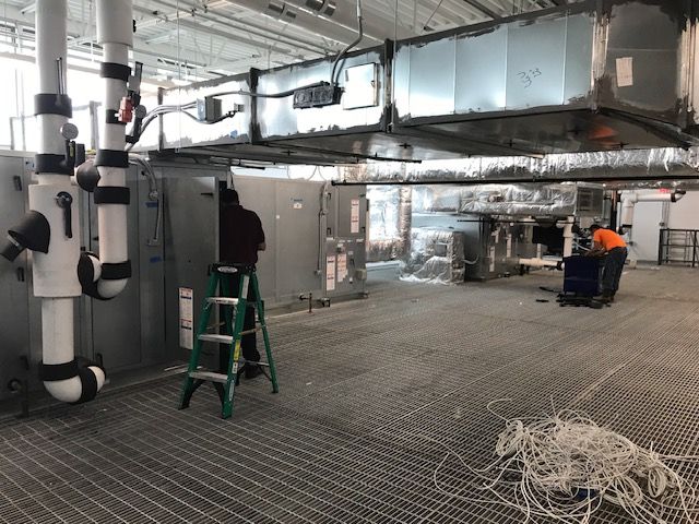 Industrial interior with exposed ductwork, a green ladder, and scattered cables on a grated floor