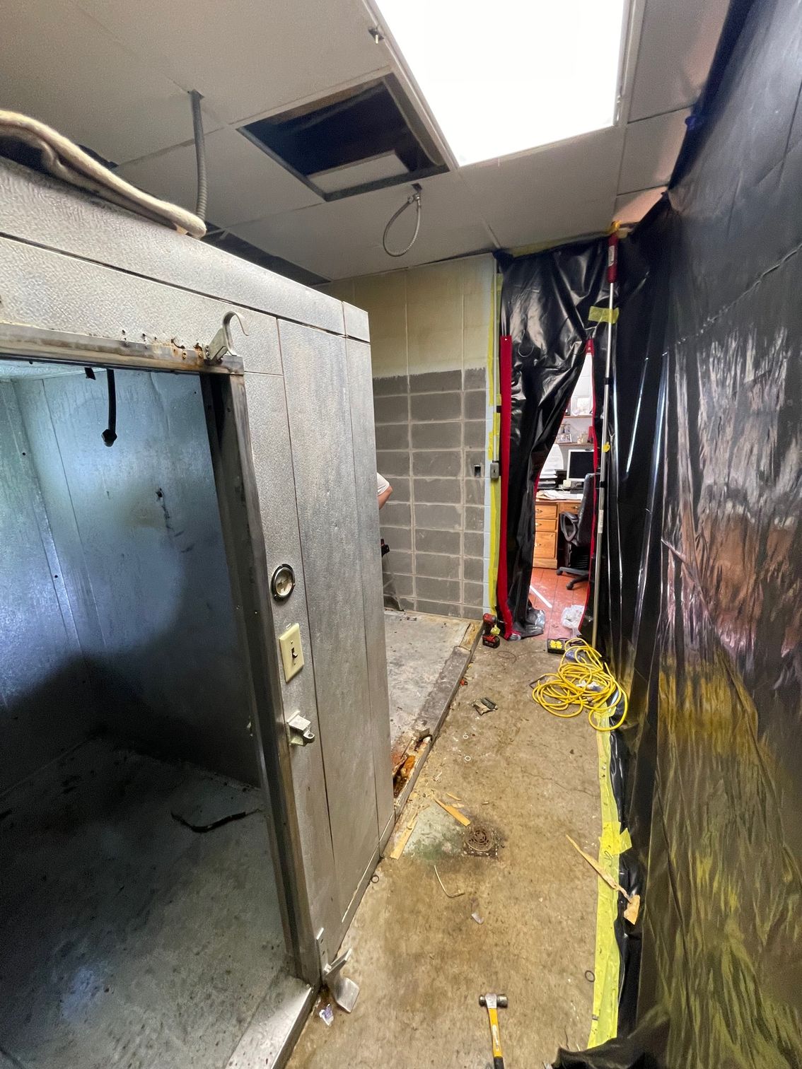 Narrow unfinished hallway with exposed ceiling, damaged wall panels, and black plastic sheeting on the right.