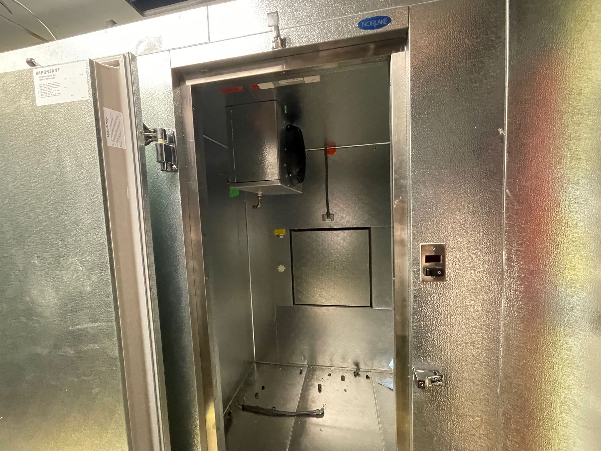 Metal commercial refrigeration unit with open door, showing empty stainless-steel interior.