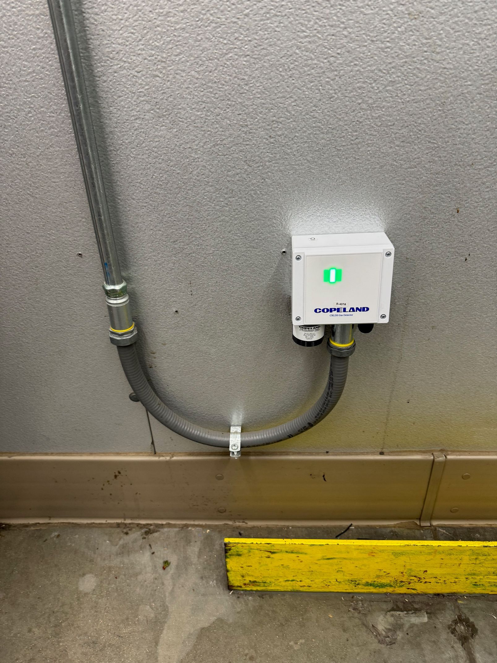 Gray wall with conduit and a small white electrical box above a yellow floor bumper.