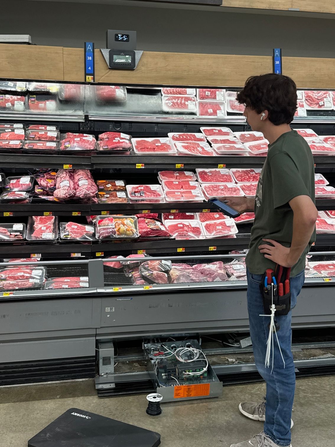 Person standing in a grocery meat aisle, looking at packaged cuts of meat on refrigerated shelves.