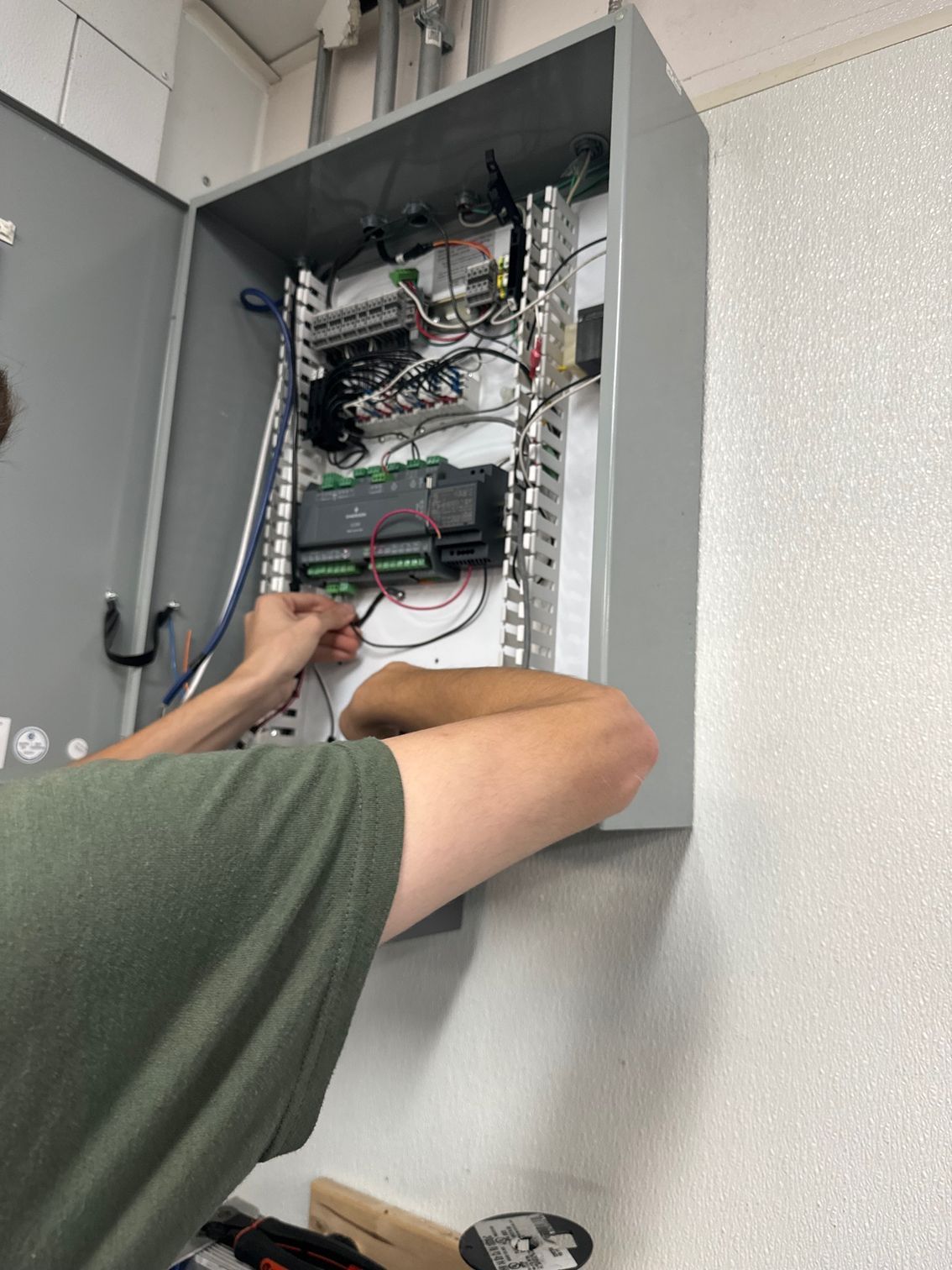 Technician wiring an open electrical control panel in a gray wall cabinet